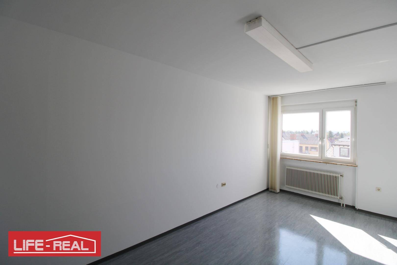 Heller Büroraum mit einem Fenster, das Tageslicht hereinlässt, und einem Heizkörper darunter.