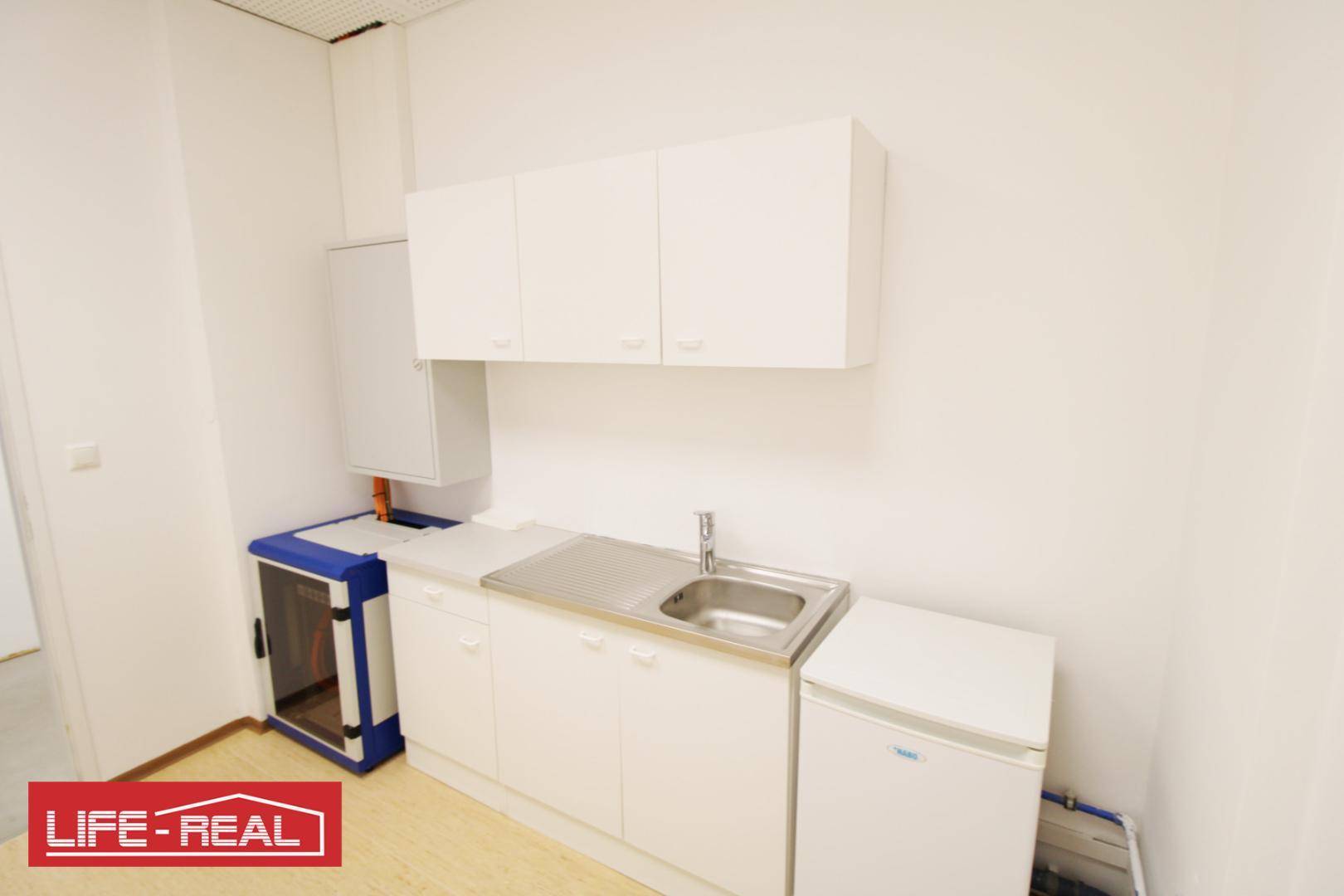 Kleine Küchenzeile mit weißen Schränken, Spüle und einem Kühlschrank in einem funktionalen Bürobereich.