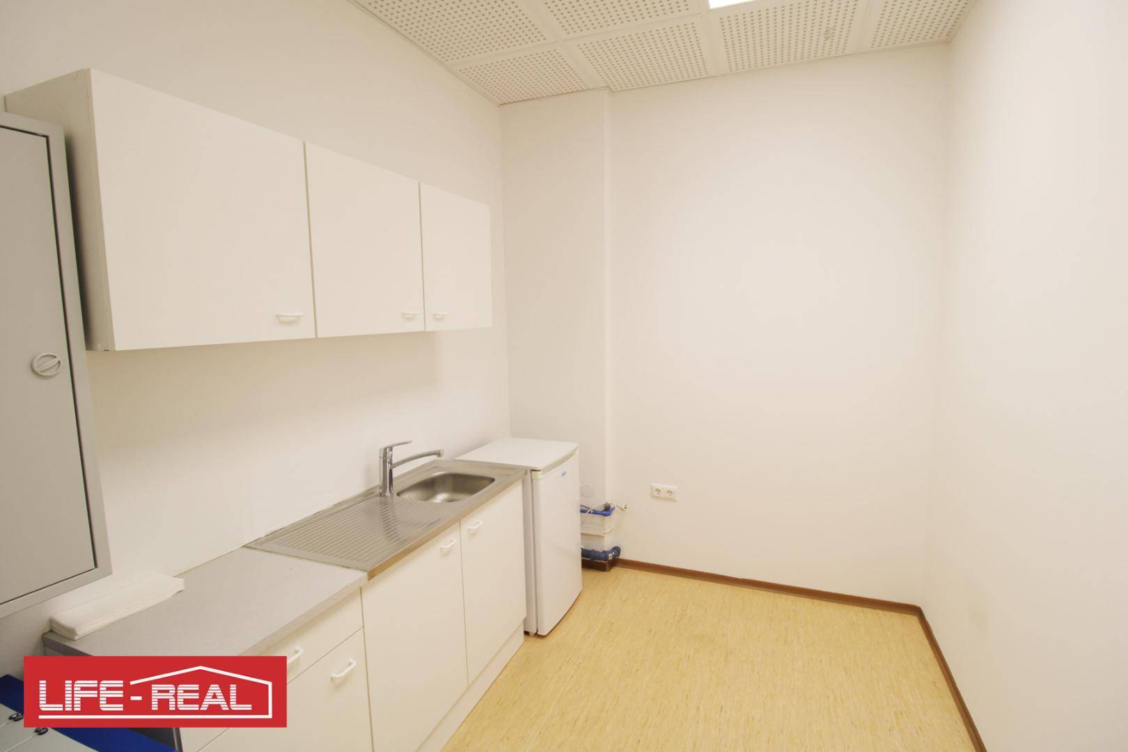 Kompakte Küchenzeile mit weißen Oberschränken, Spülbecken und einem kleinen Kühlschrank, ideal für Büros.