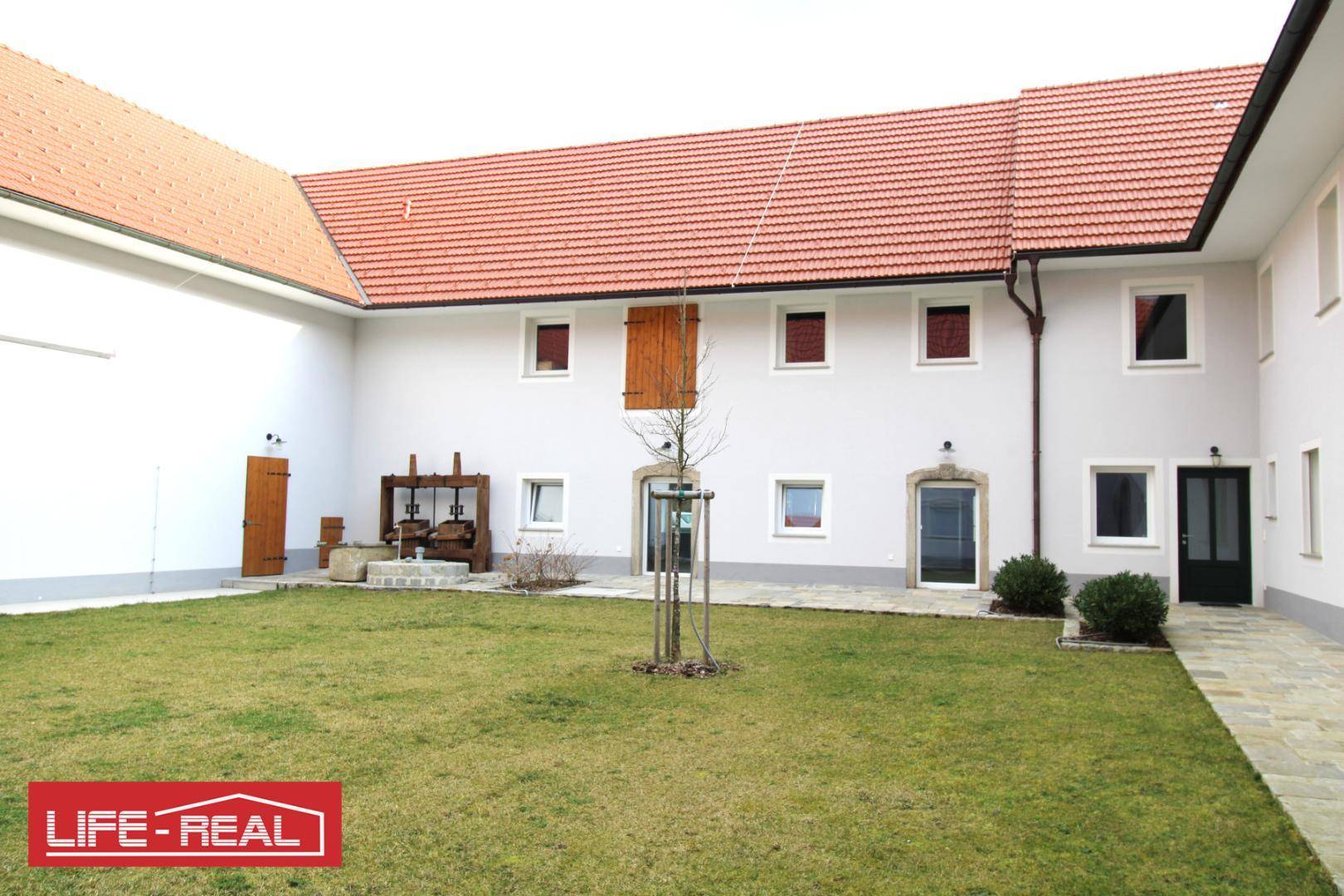 Grüner Innenhof mit Rasenfläche und traditioneller Architektur, umgeben von Gebäudeflügeln.