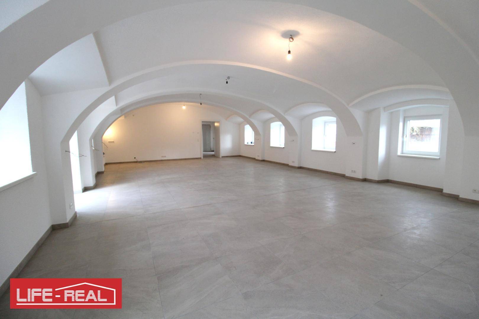 Weitläufiger Innenraum mit markanten Gewölbedecken und großen Fenstern, ideal für offene Konzepte.