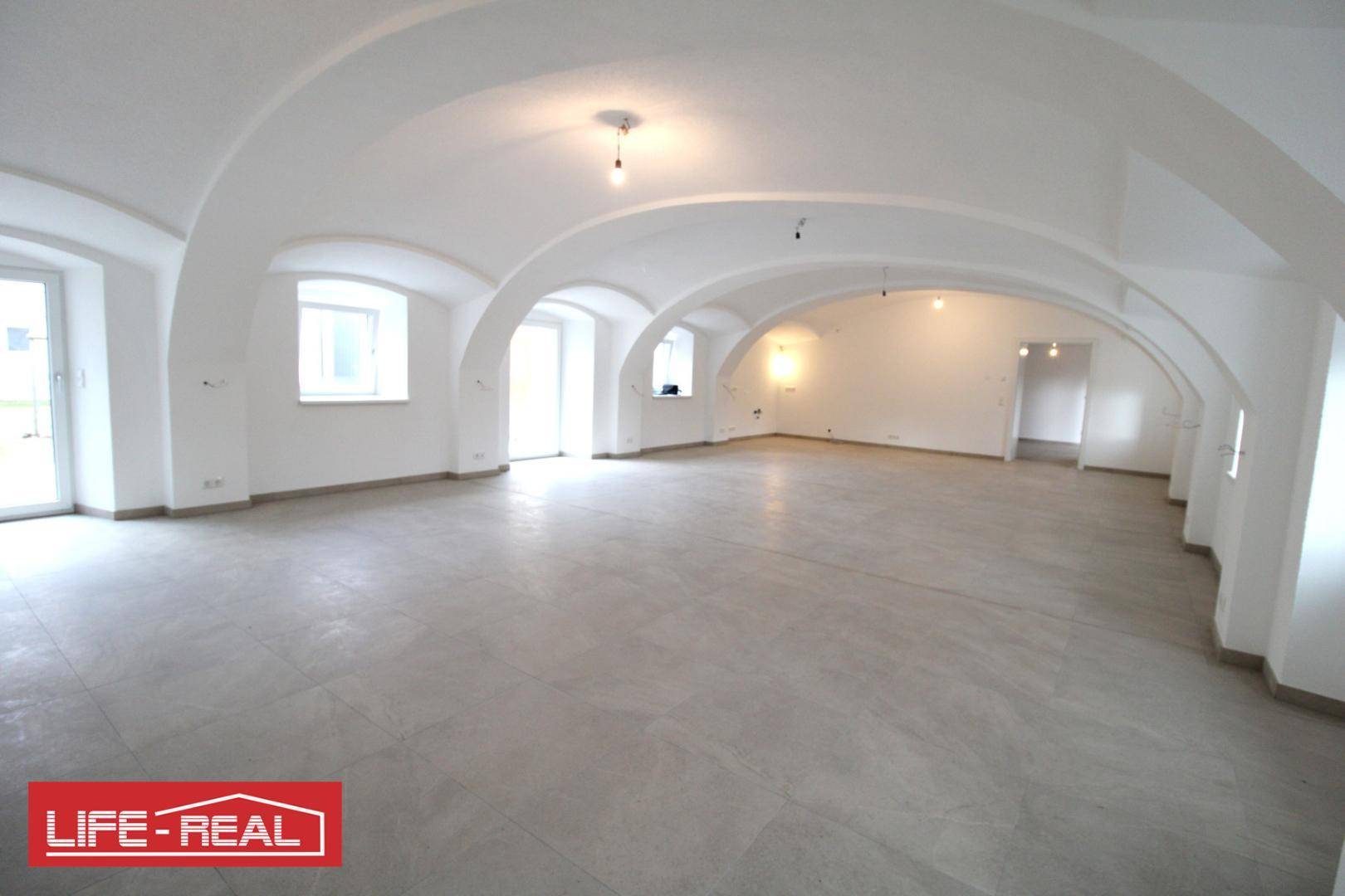 Großer, heller Raum mit beeindruckenden Gewölbedecken und mehreren Fenstern, unmöbliert.