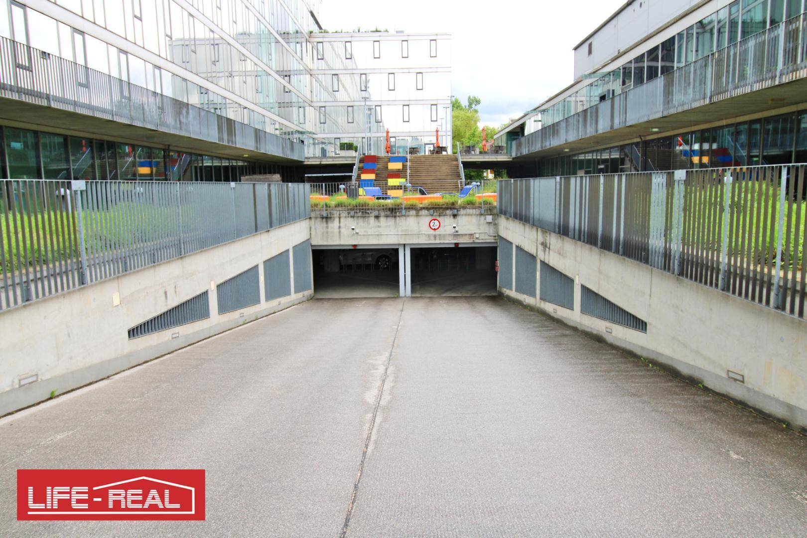 Zufahrt zu einer Tiefgarage zwischen modernen Gebäuden, mit klaren Markierungen für die Einfahrt.