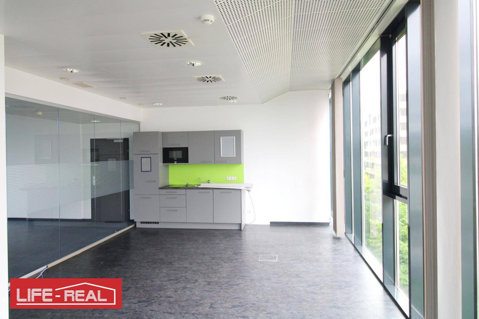 Moderne Teeküche mit grauen Schränken und grüner Rückwand, ideal für kurze Pausen im Büro.