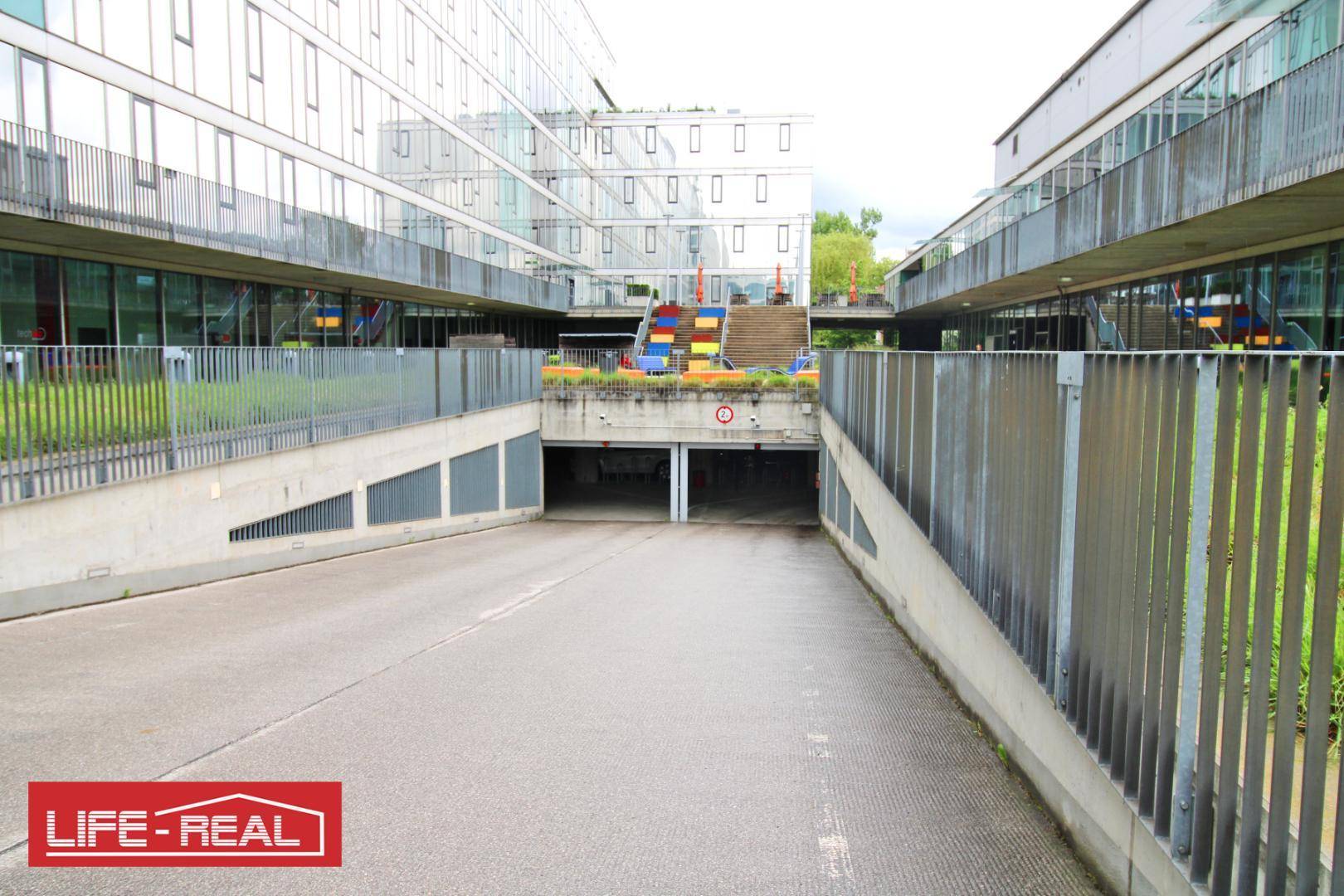 Zufahrt zu einer Tiefgarage zwischen modernen Gebäuden, bietet bequemen Zugang zu Parkplätzen.