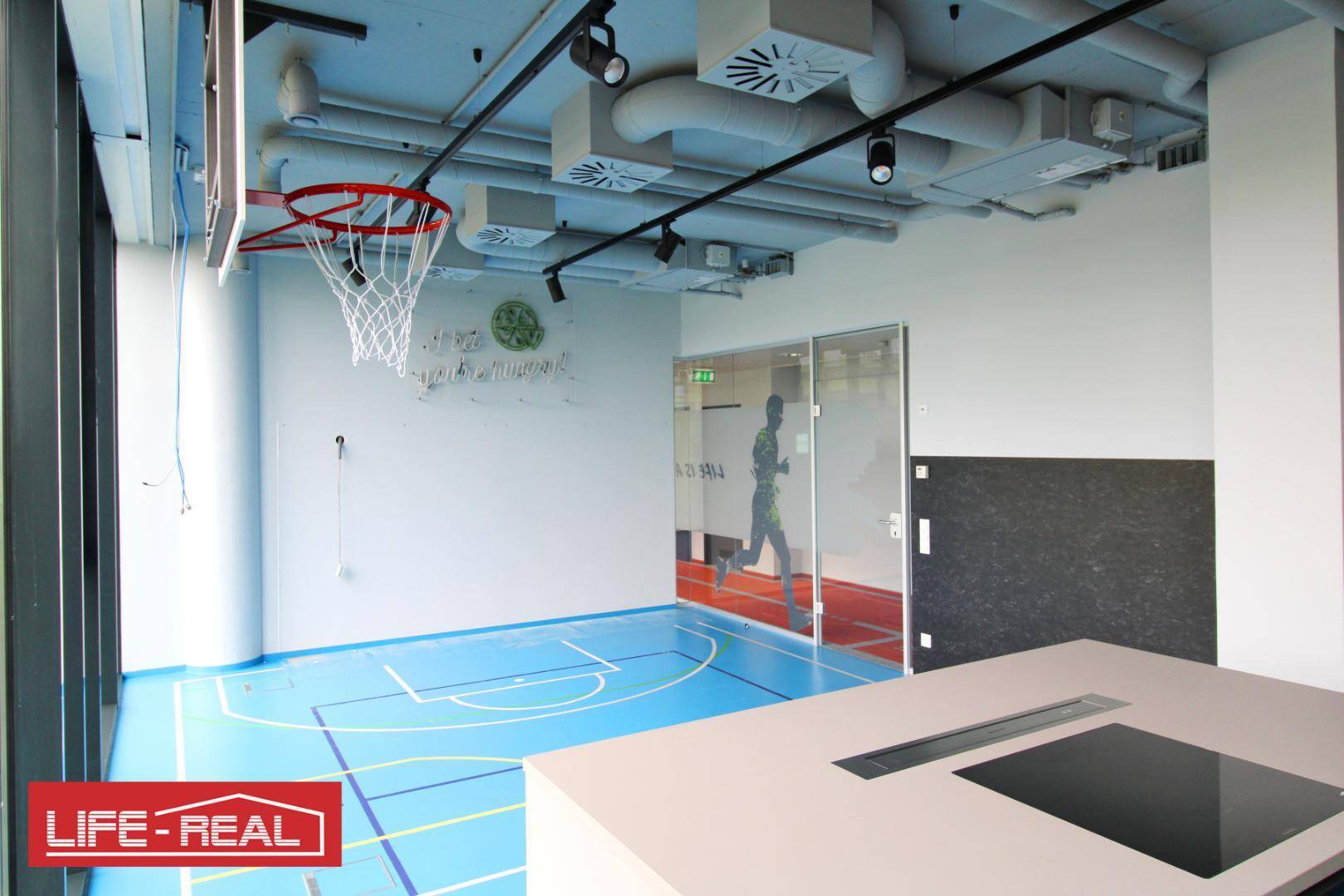 Büroküche mit blauer Sportboden und Basketballkorb, ausgestattet mit modernen Küchengeräten und viel Licht.