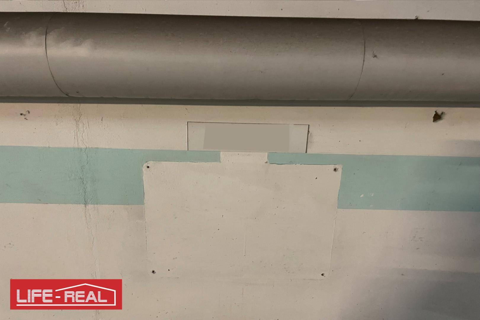 Detailansicht einer Wand in der Tiefgarage mit blauer Markierung und sichtbaren Rohren.