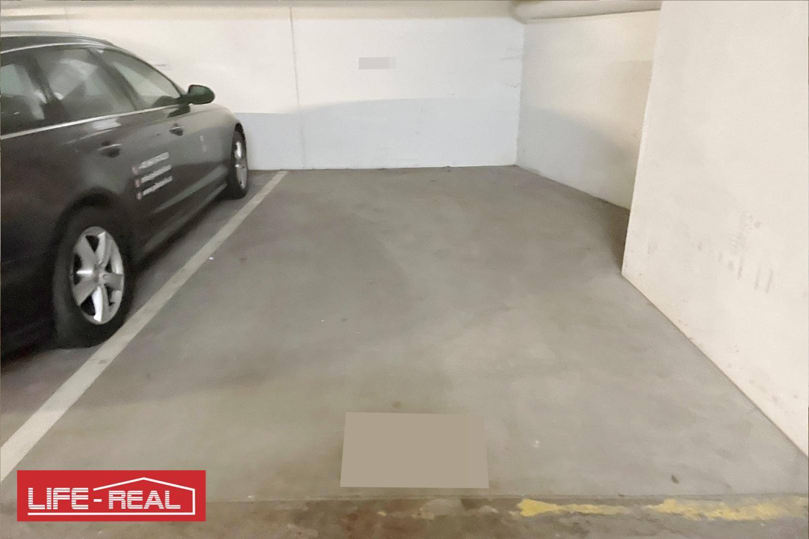 Einzelner Tiefgaragenstellplatz mit einem geparkten Fahrzeug und Betonboden.