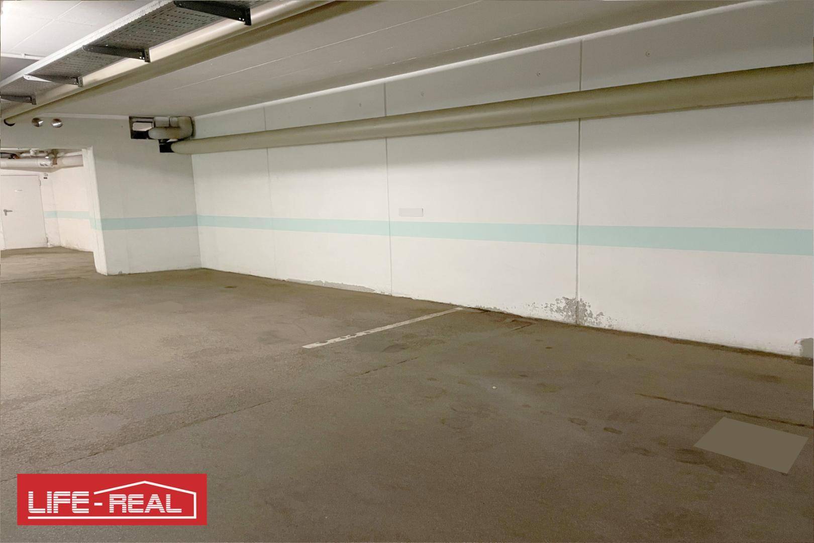 Geräumiger Tiefgaragenstellplatz mit Betonboden und sichtbaren Leitungen an der Decke.