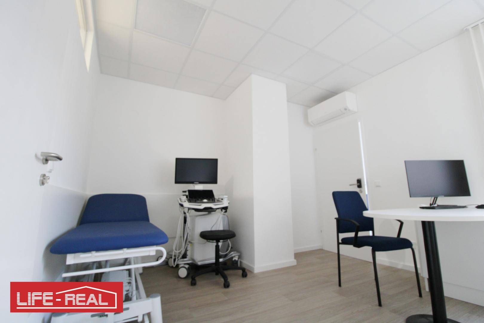 Heller Behandlungsraum mit Untersuchungsliege und medizinischen Geräten, bereit für Patienten.