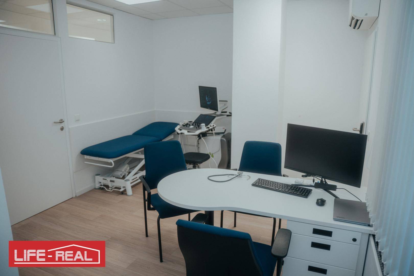Medizinischer Behandlungsraum mit Untersuchungsliege, Schreibtisch und moderner Ausstattung für Patienten.