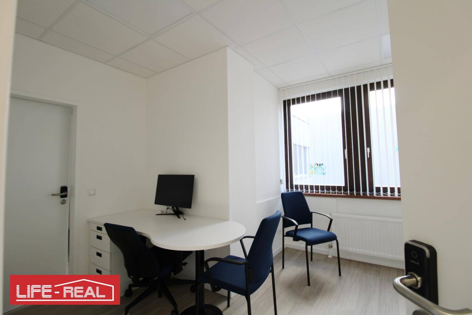 Helles Beratungszimmer mit modernem Schreibtisch, Stühlen und einem Fenster mit Jalousien.