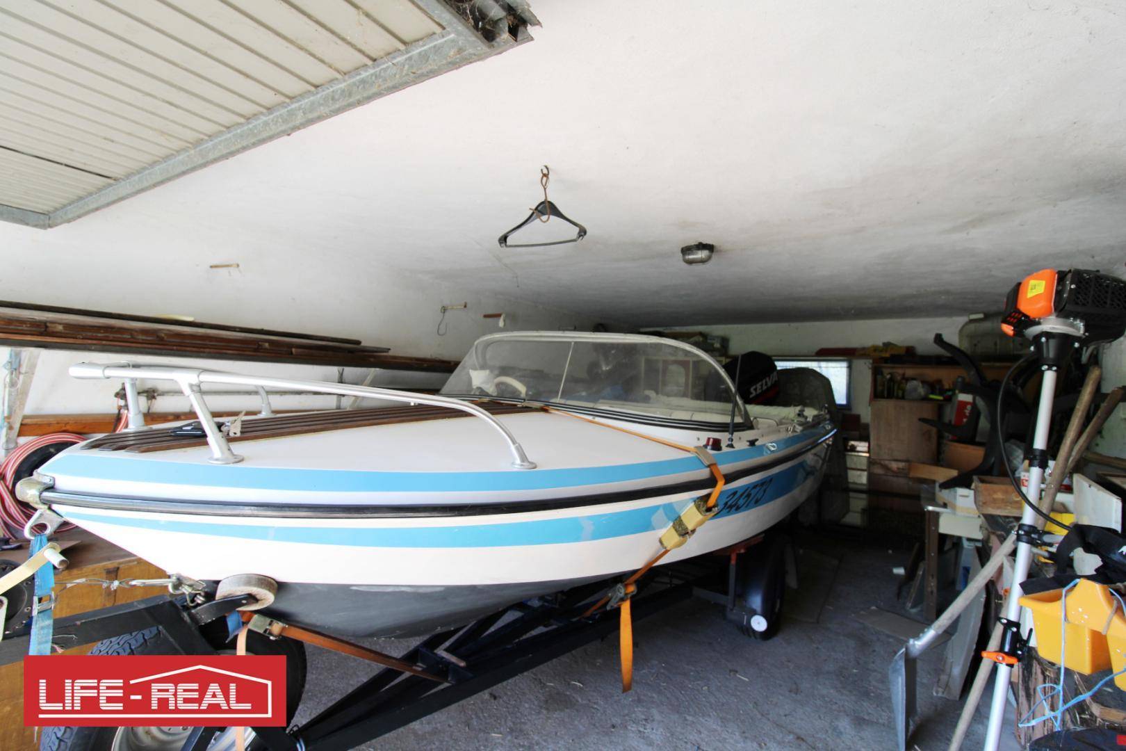 Geräumige Garage mit einem Boot auf einem Anhänger und verschiedenen Werkzeugen.