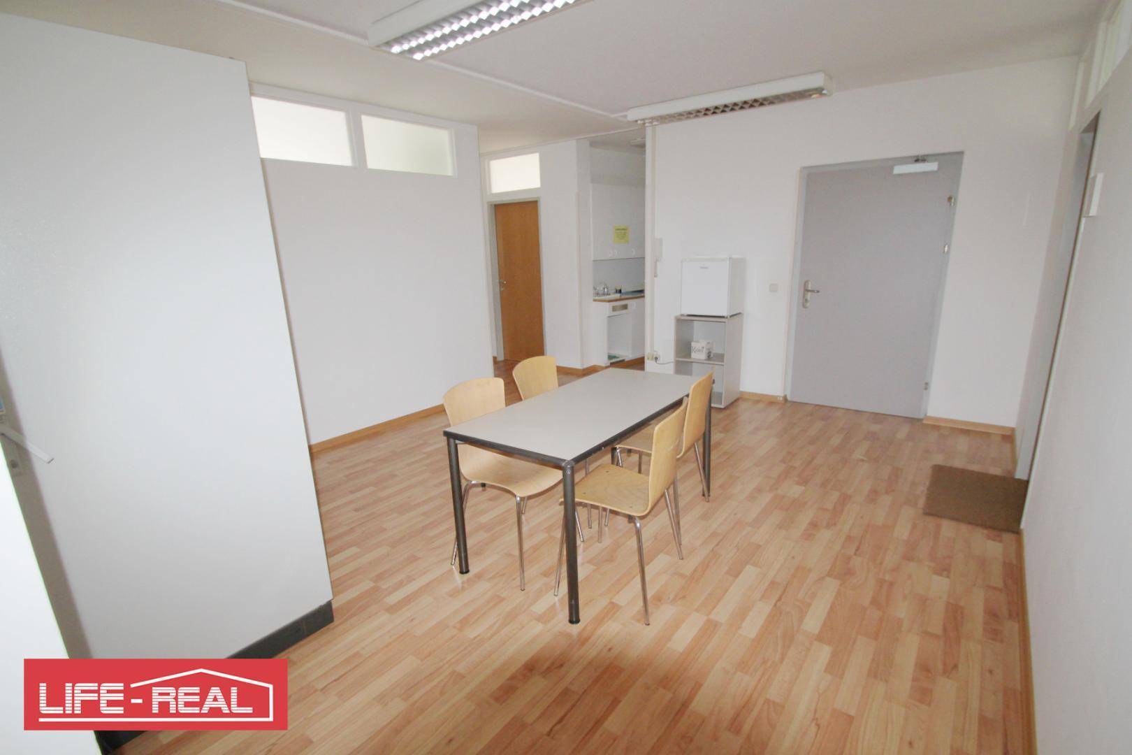 Übersicht des Pausenraums mit Esstisch, Kühlschrank und kleiner Küchenzeile im Hintergrund.