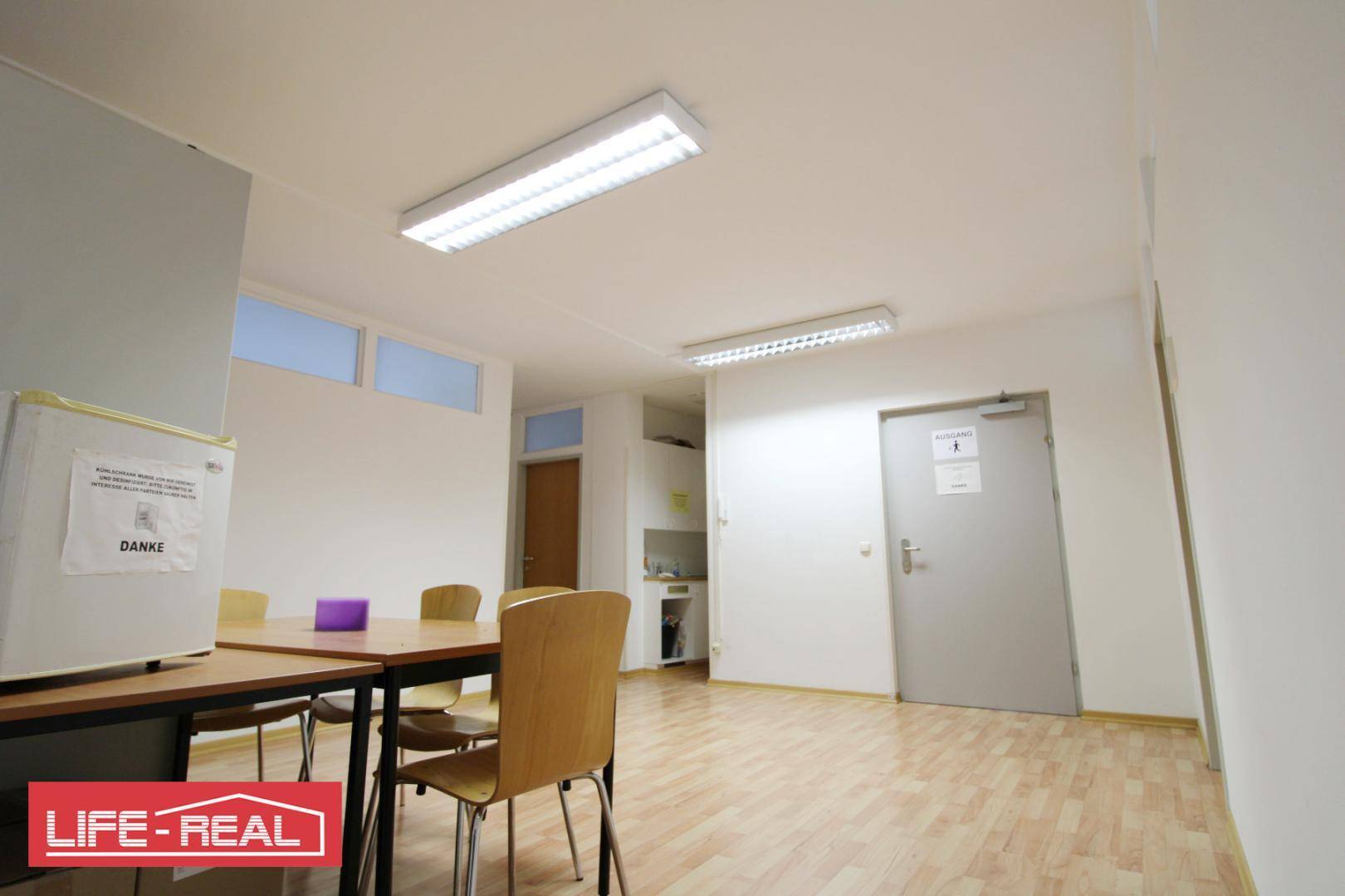 Gemeinschaftsraum mit Tisch, Stühlen und Kühlschrank, ideal für Pausen oder Besprechungen.