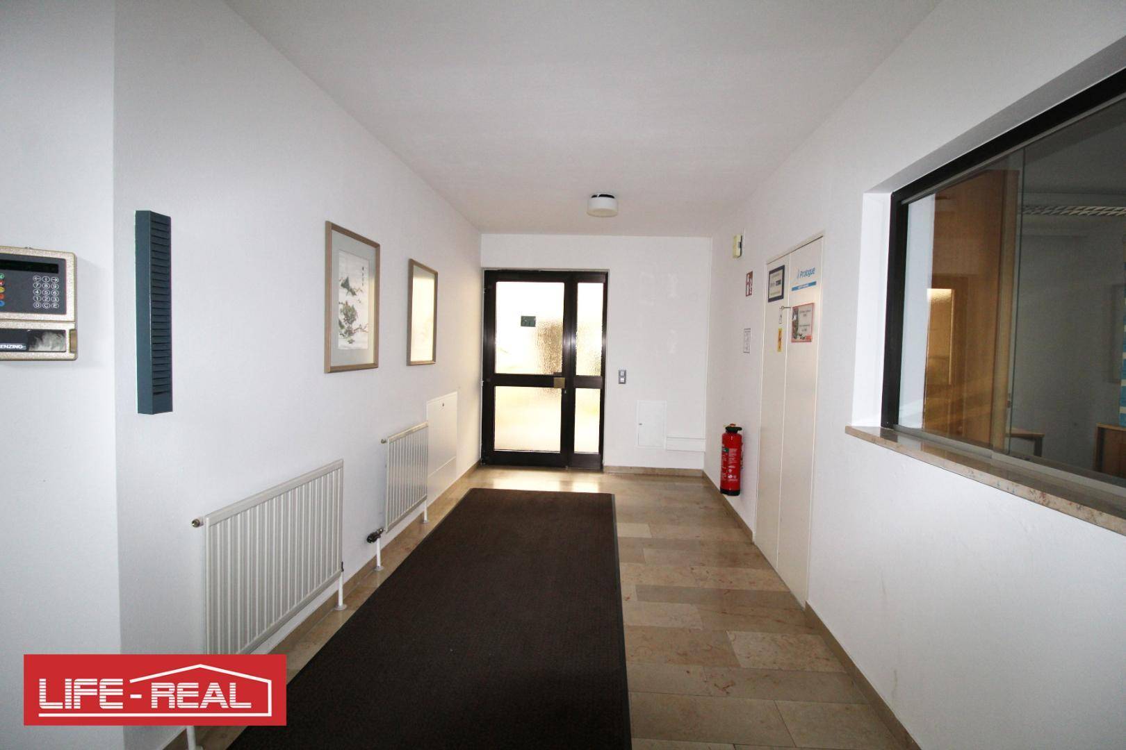 Heller Flur mit Fliesenboden, Heizkörpern und einem Fenster, das Tageslicht hereinlässt.