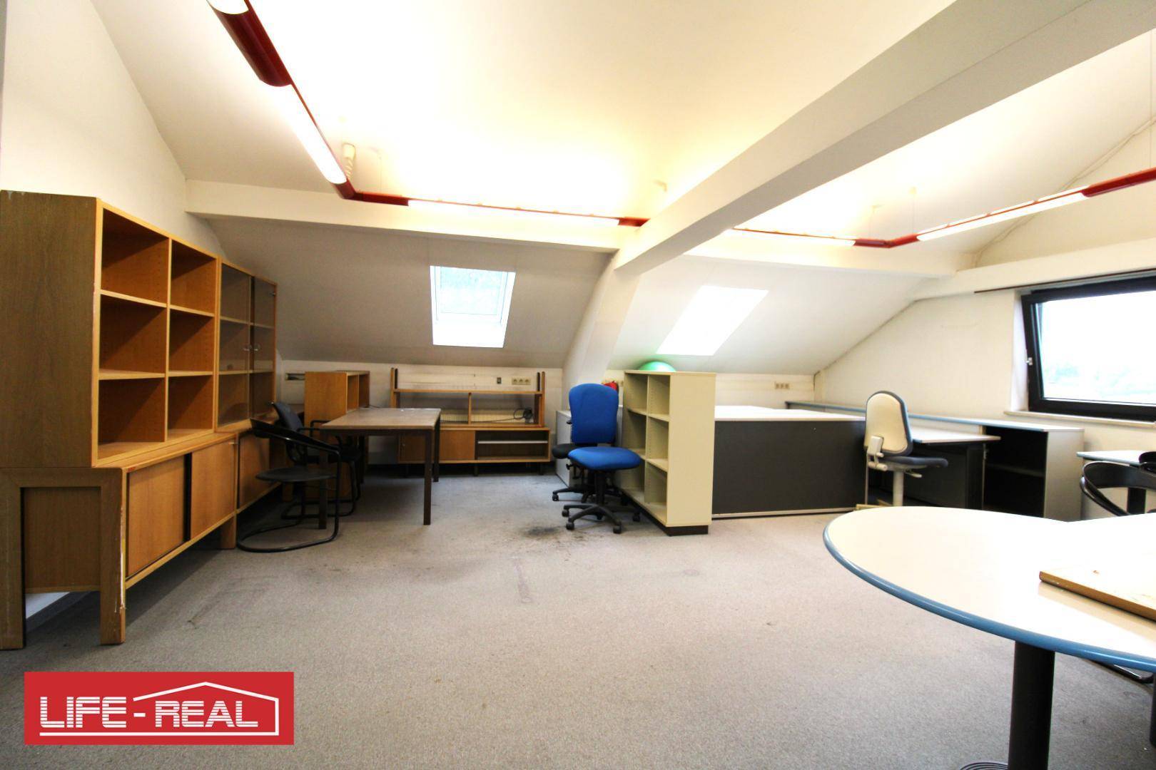 Geräumiges Dachgeschossbüro mit verschiedenen Arbeitsbereichen, Regalen und Schreibtischen, hell und funktional.