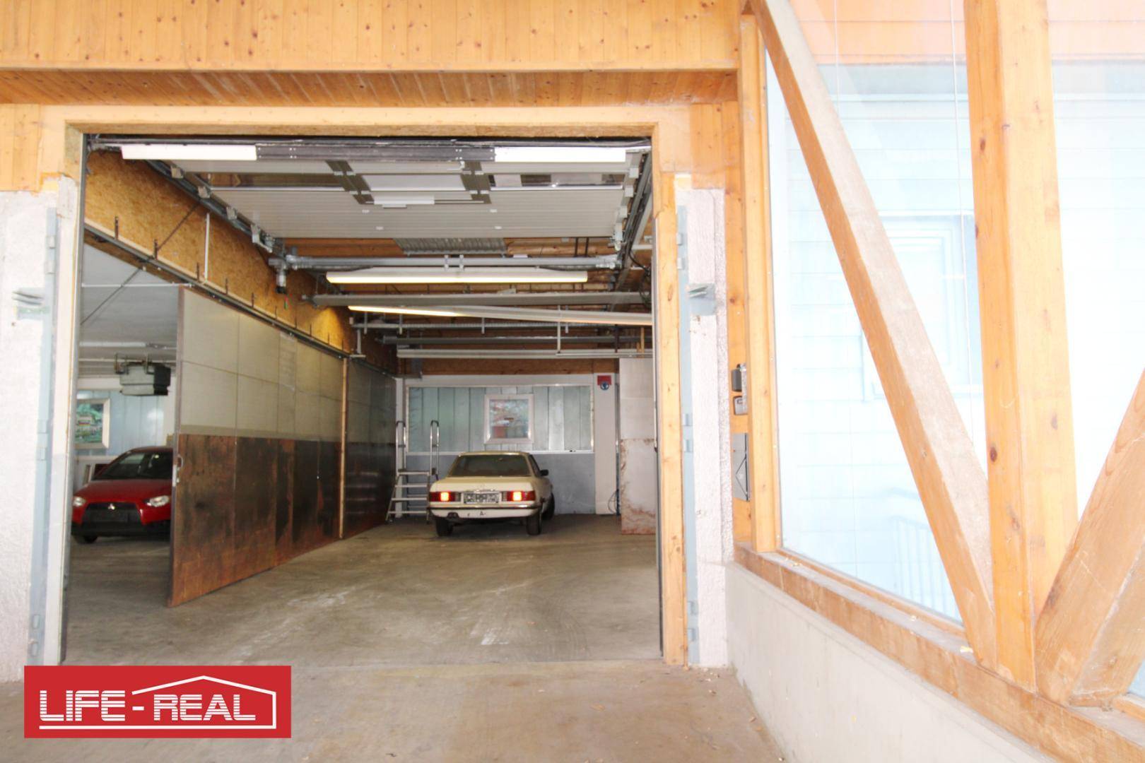 Innenansicht einer Garage oder Lagerhalle mit geparkten Autos und Holzbalken.