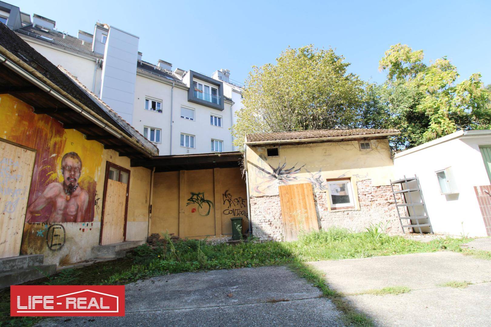 Blick auf den Hinterhofbereich mit Nebengebäude und weiteren Graffitis an den Wänden des alten Gebäudes.