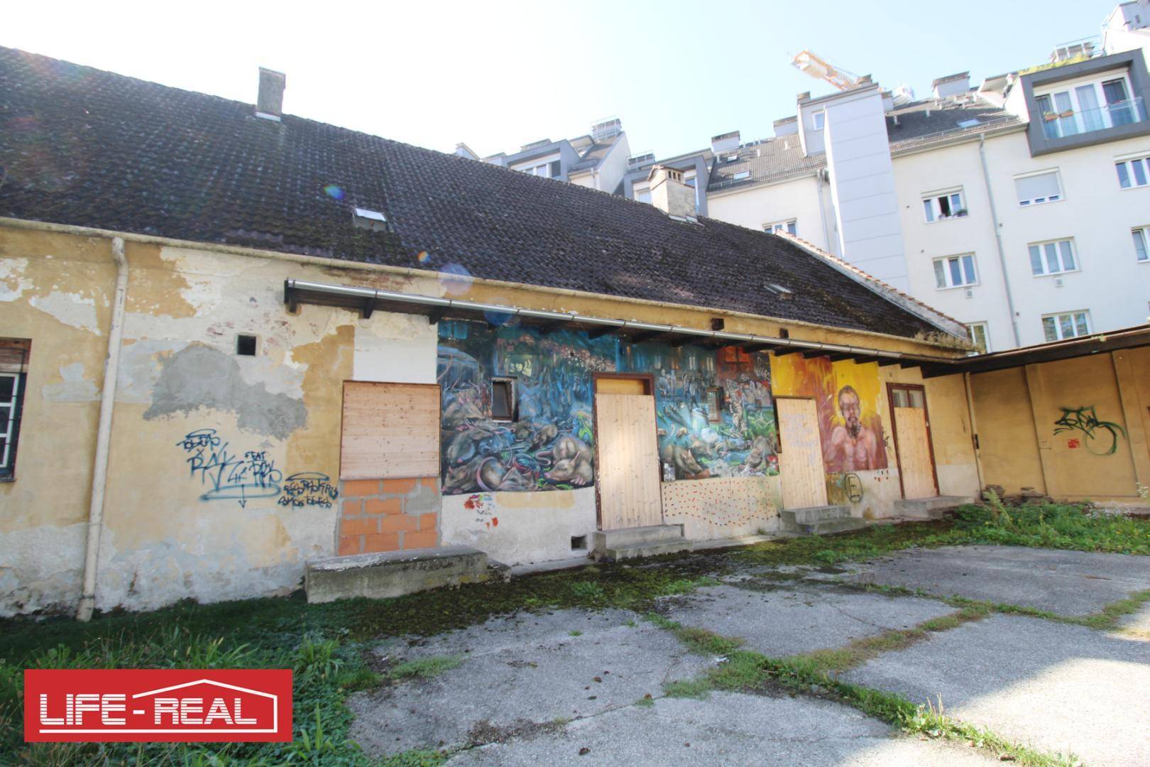 Seitenansicht des alten Gebäudes mit umfangreichen Graffitis und zugenagelten Öffnungen im Sonnenlicht.