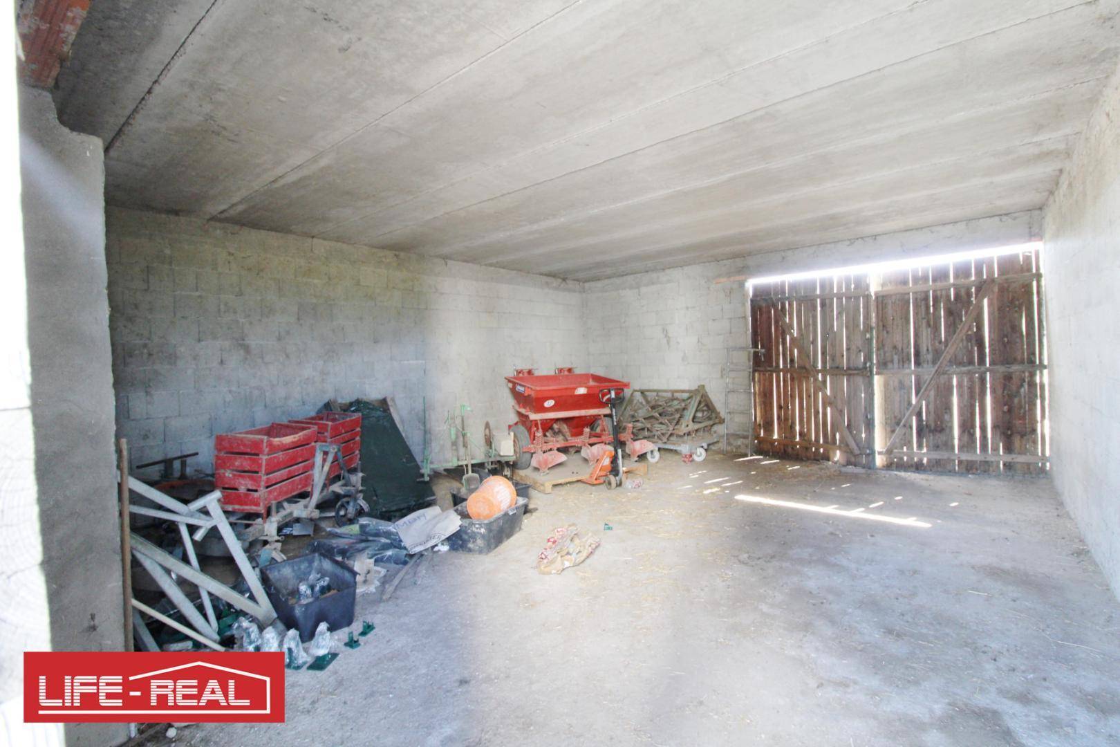 Geräumiger Lagerraum mit Betonwänden und -decke, gefüllt mit landwirtschaftlichen Geräten und Werkzeugen.