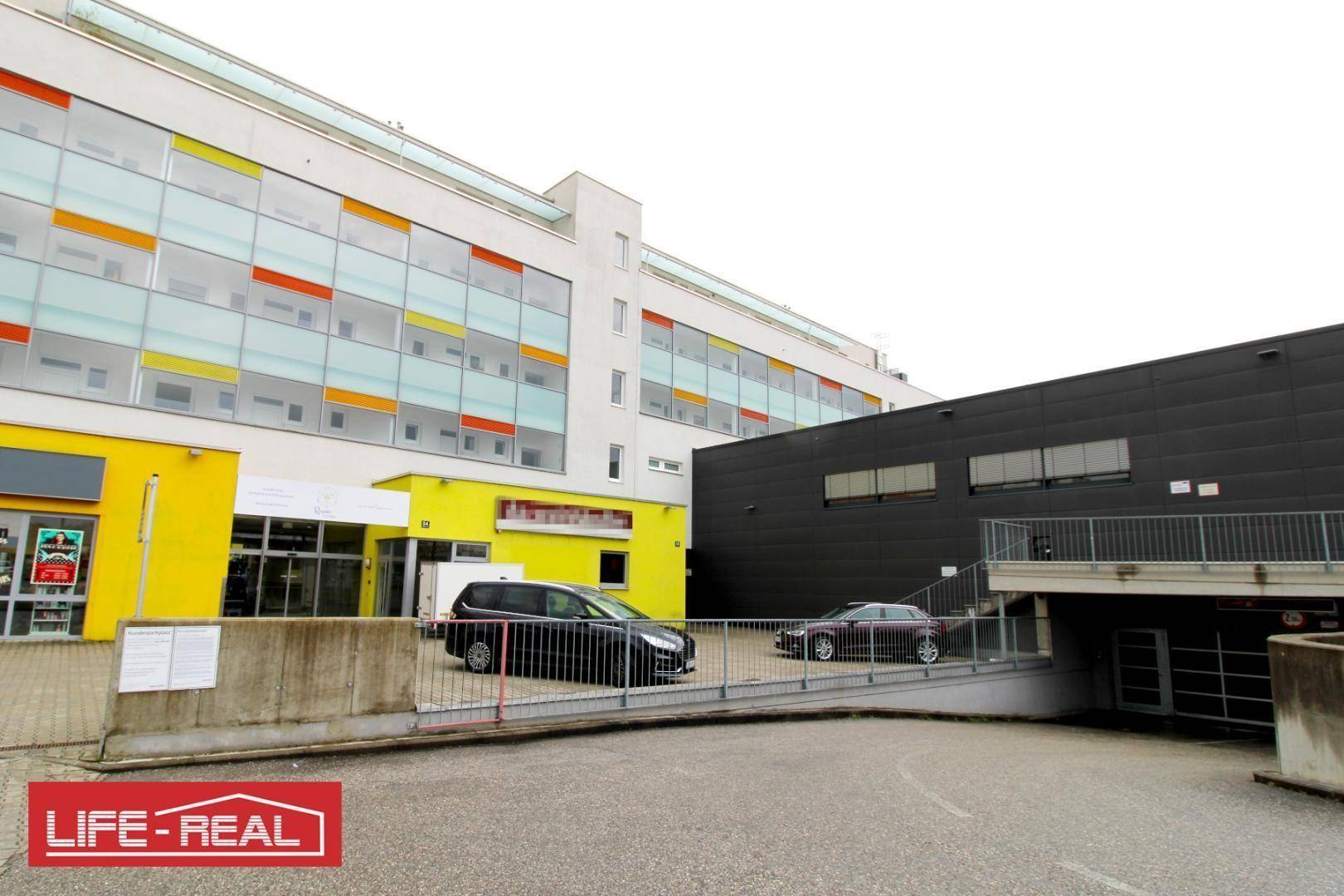 Gebäudekomplex mit Tiefgaragenzufahrt und moderner Fassade mit farbigen Fenstern.