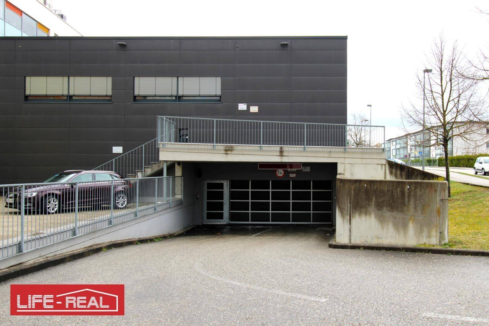 Außenzugang zu einer Tiefgarage mit Rampe und angrenzendem Gebäude.