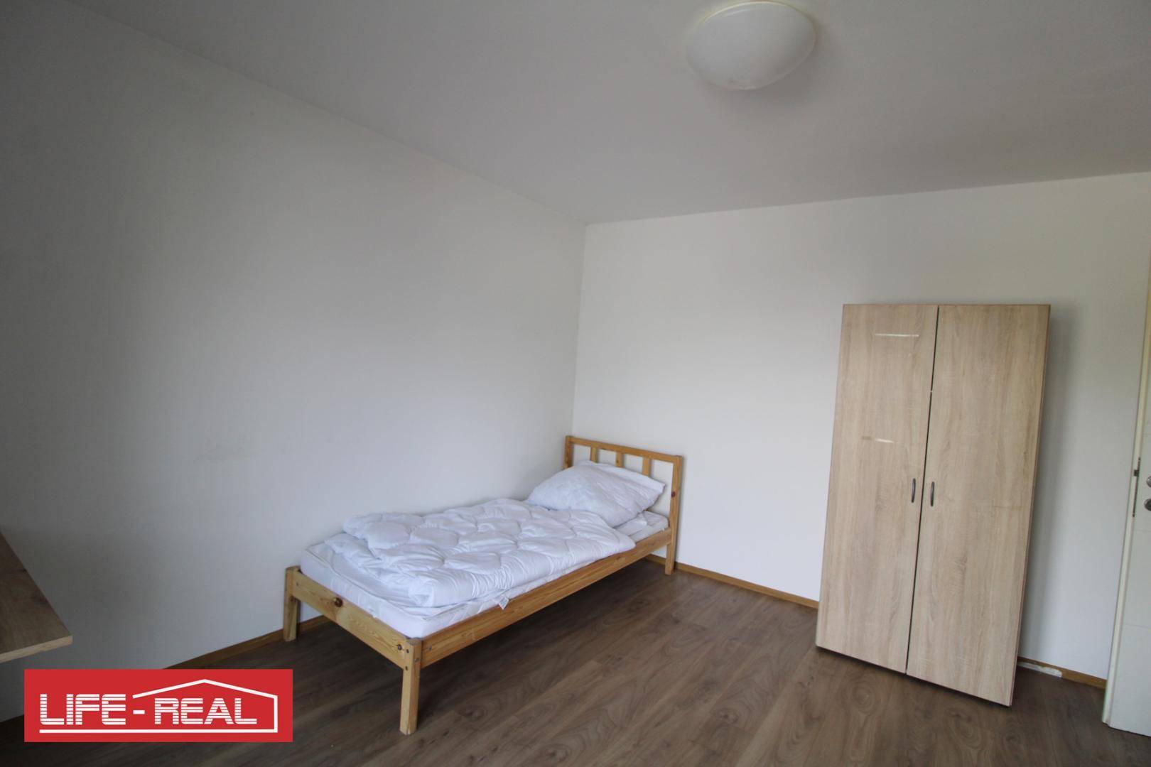 Einfaches Schlafzimmer mit Einzelbett, hellem Kleiderschrank und Holzboden.