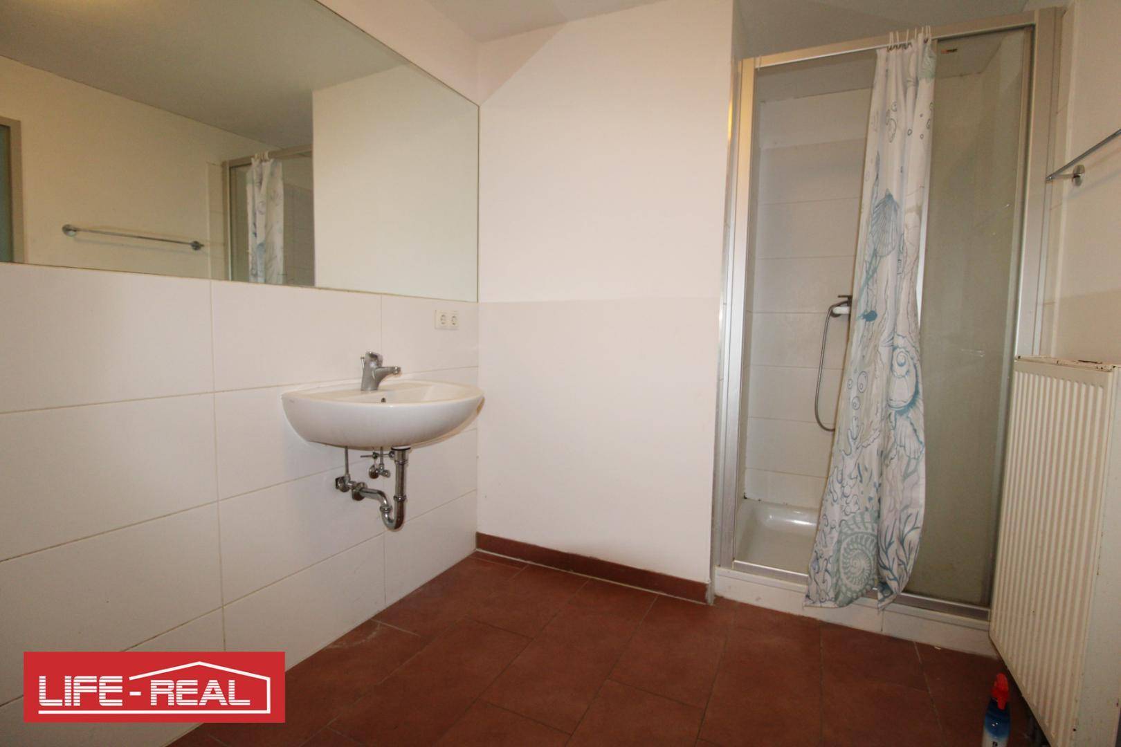 Badezimmer mit Waschbecken, großem Spiegel und einer Duschkabine, ausgestattet mit braunen Fliesen.