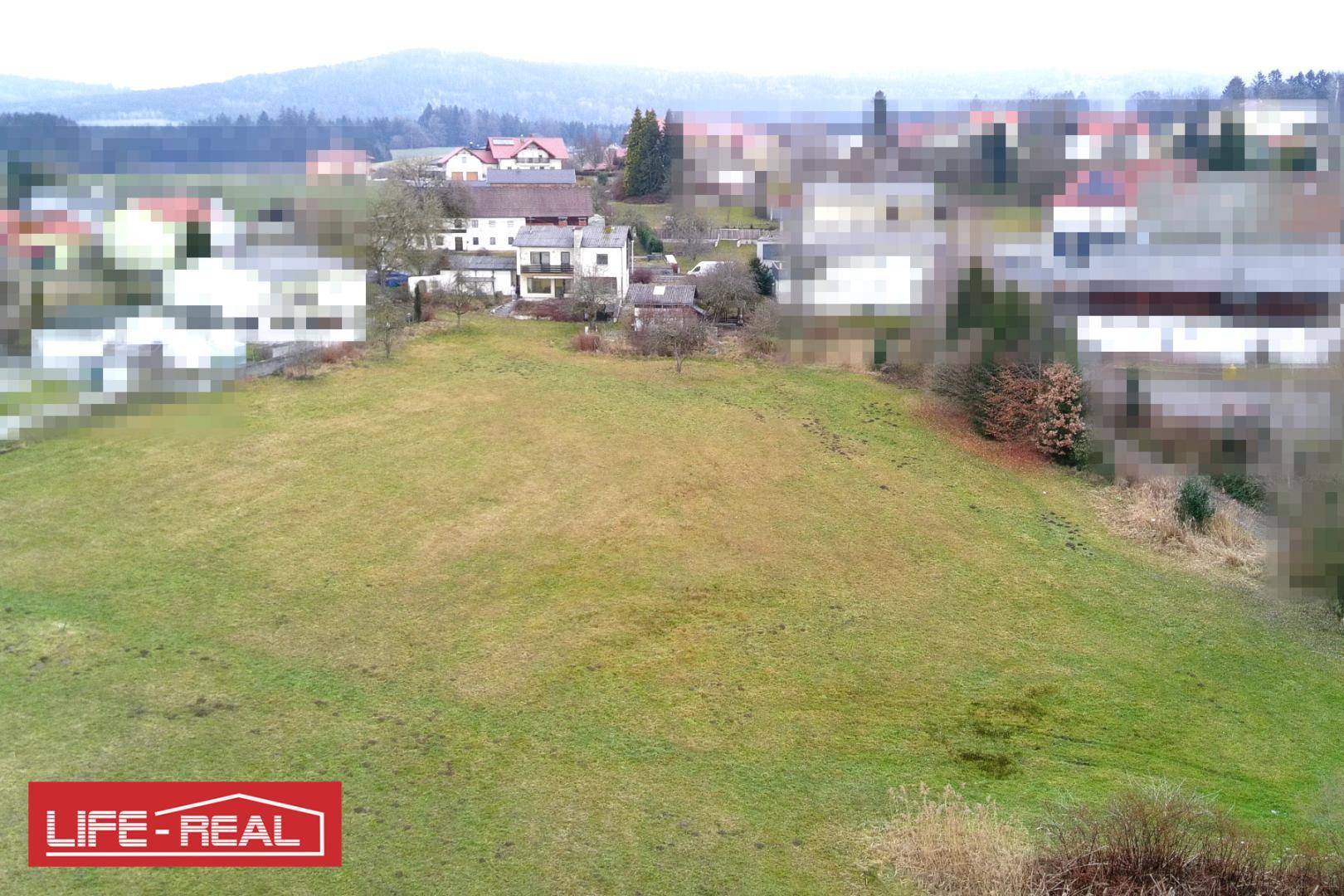 Weitläufige grüne Landschaft mit unscharfem Blick auf entfernte Häuser und Hügel.