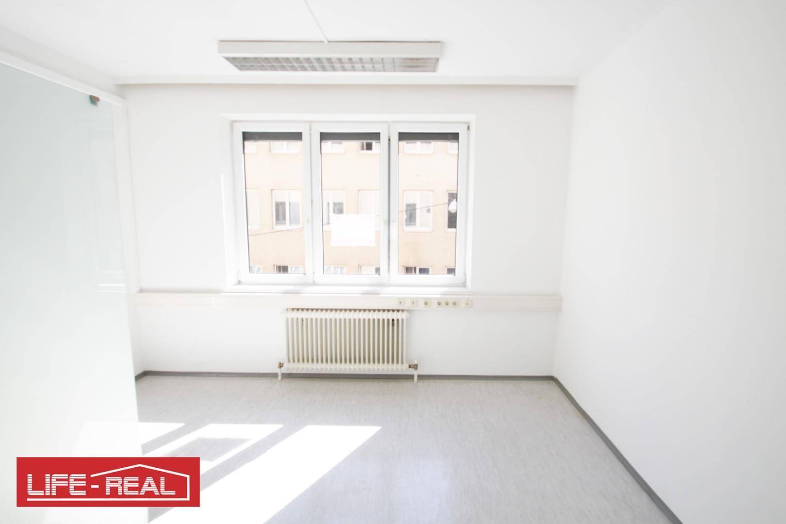 Heller Büroraum mit großem Fenster, das viel Tageslicht hereinlässt, und einem Heizkörper.
