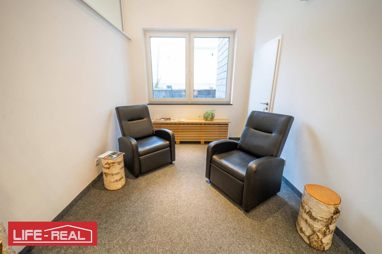 Gemütlicher Wartebereich mit zwei schwarzen Ledersesseln, Teppichboden und einem Fenster für Tageslicht.