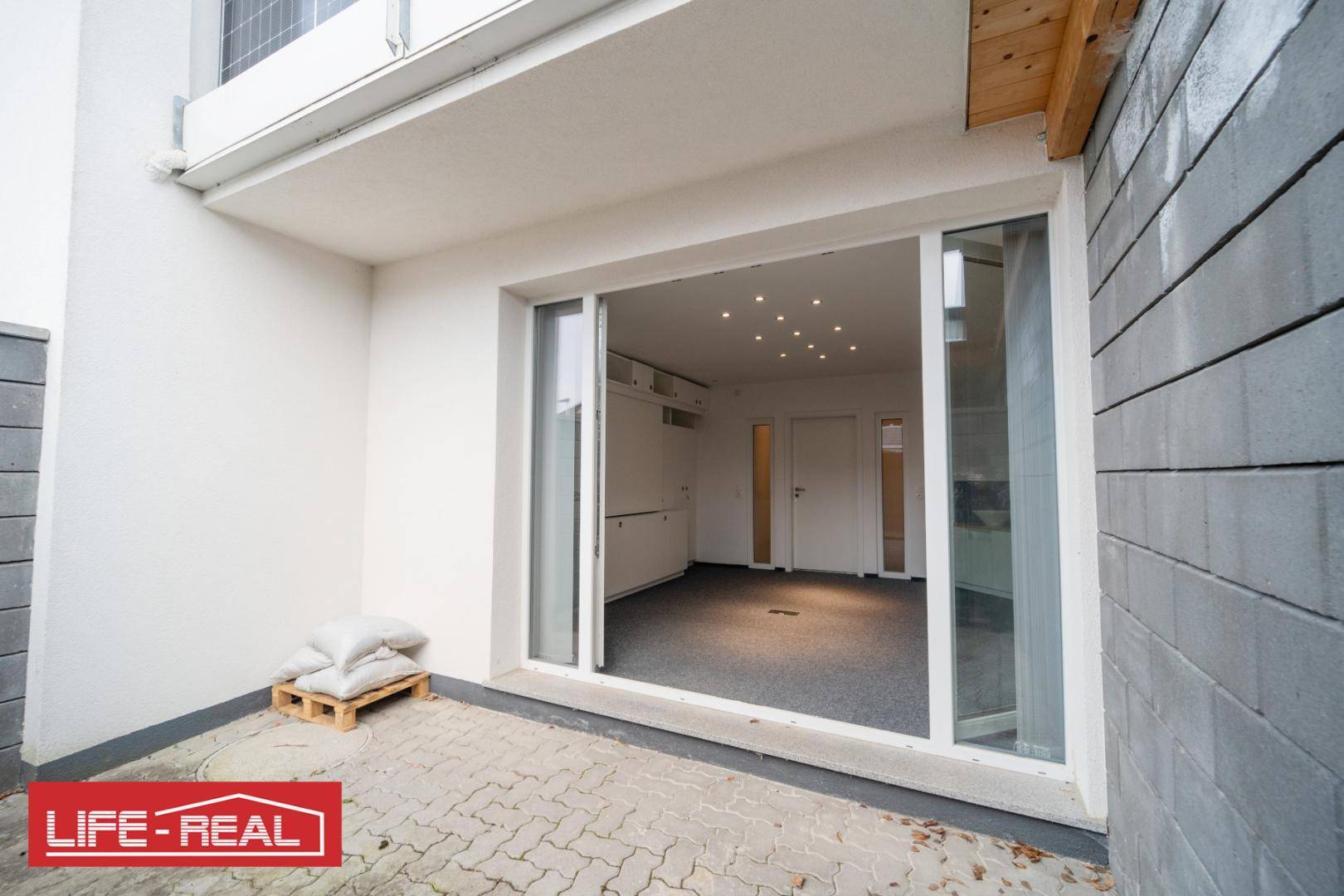 Außenbereich mit gepflasterter Terrasse und großen Schiebetüren, die in einen modernen Innenraum führen.