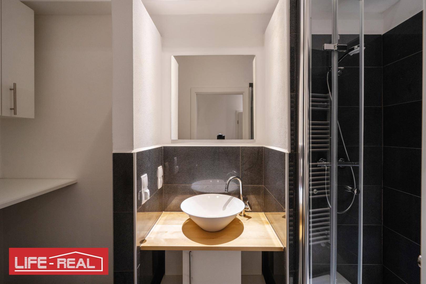Modernes Badezimmer mit Waschbecken, Holzplatte, Spiegel und einer Duschkabine, stilvoll gestaltet.