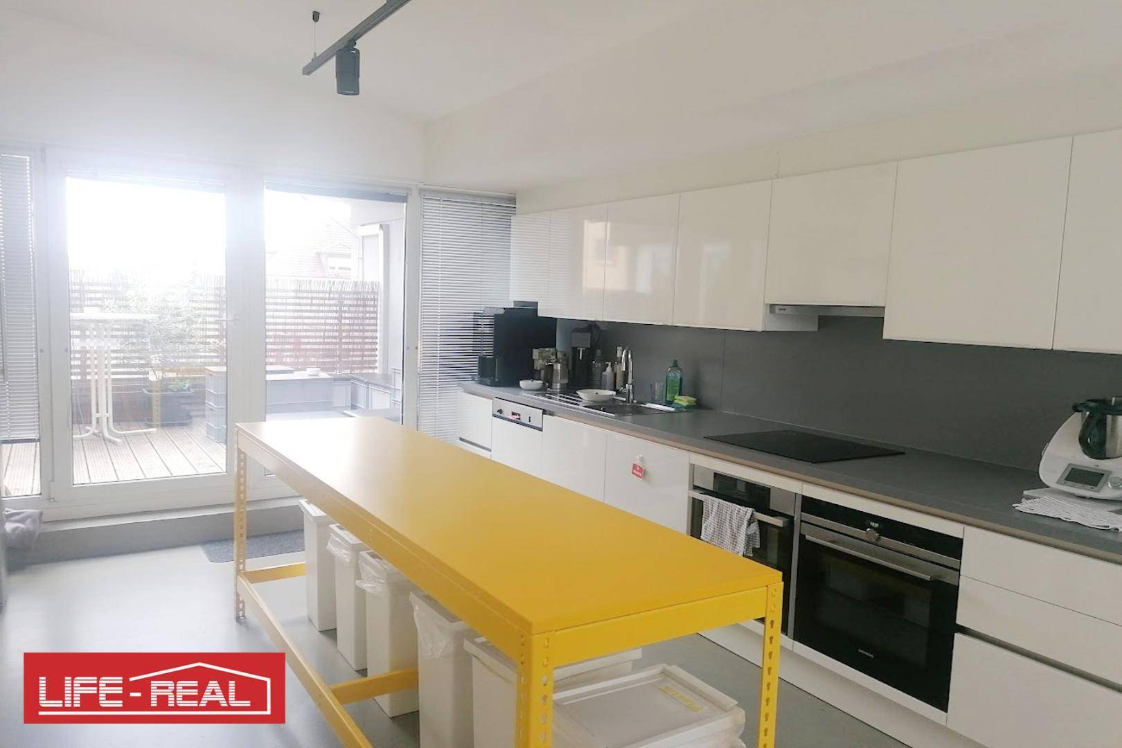 Moderne Küche mit weißen Hochglanzschränken, Induktionskochfeld und Zugang zu einer Terrasse.