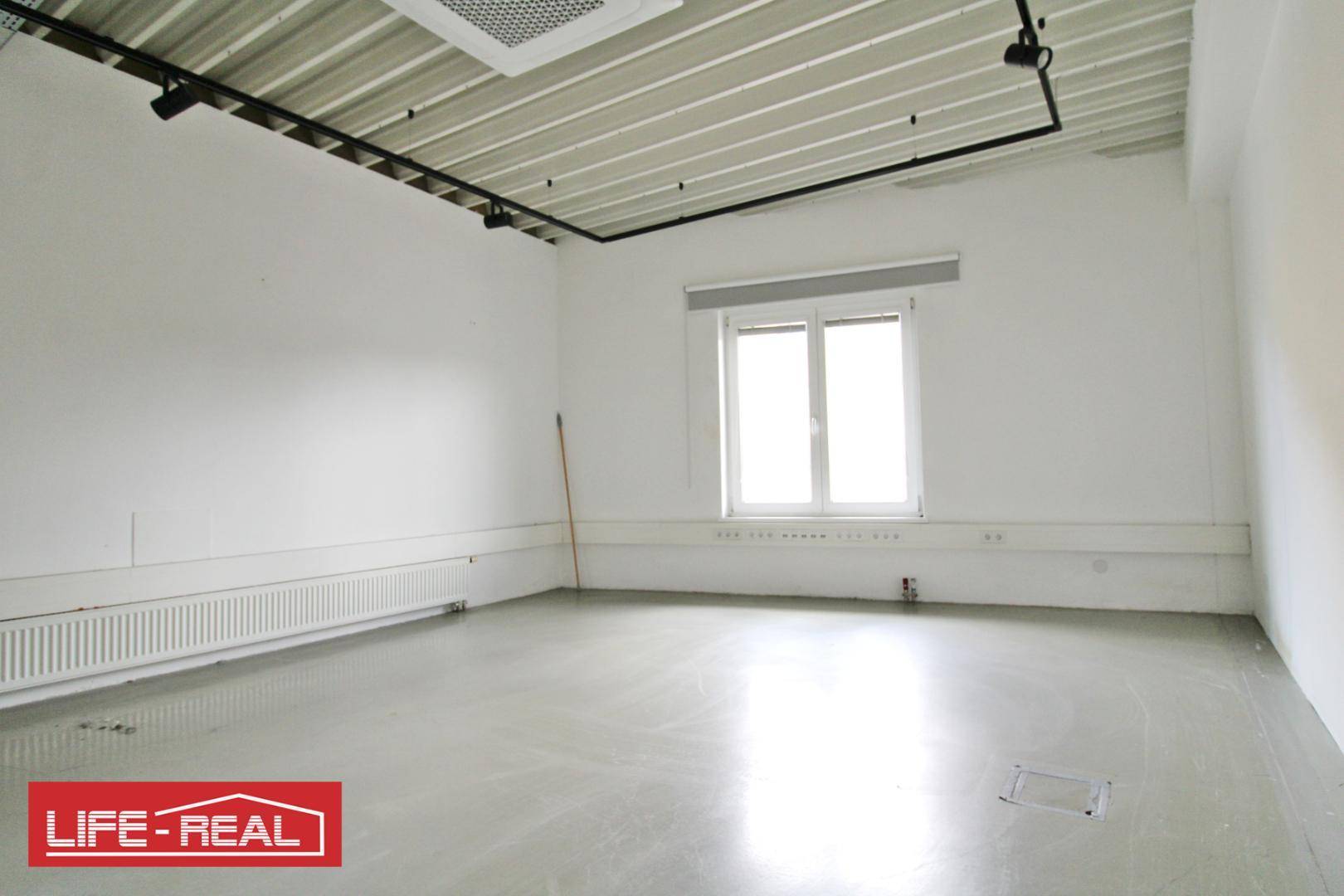 Schlichter Büroraum mit weiß gestrichenen Wänden, Betonboden und einem Fenster mit Rollo.