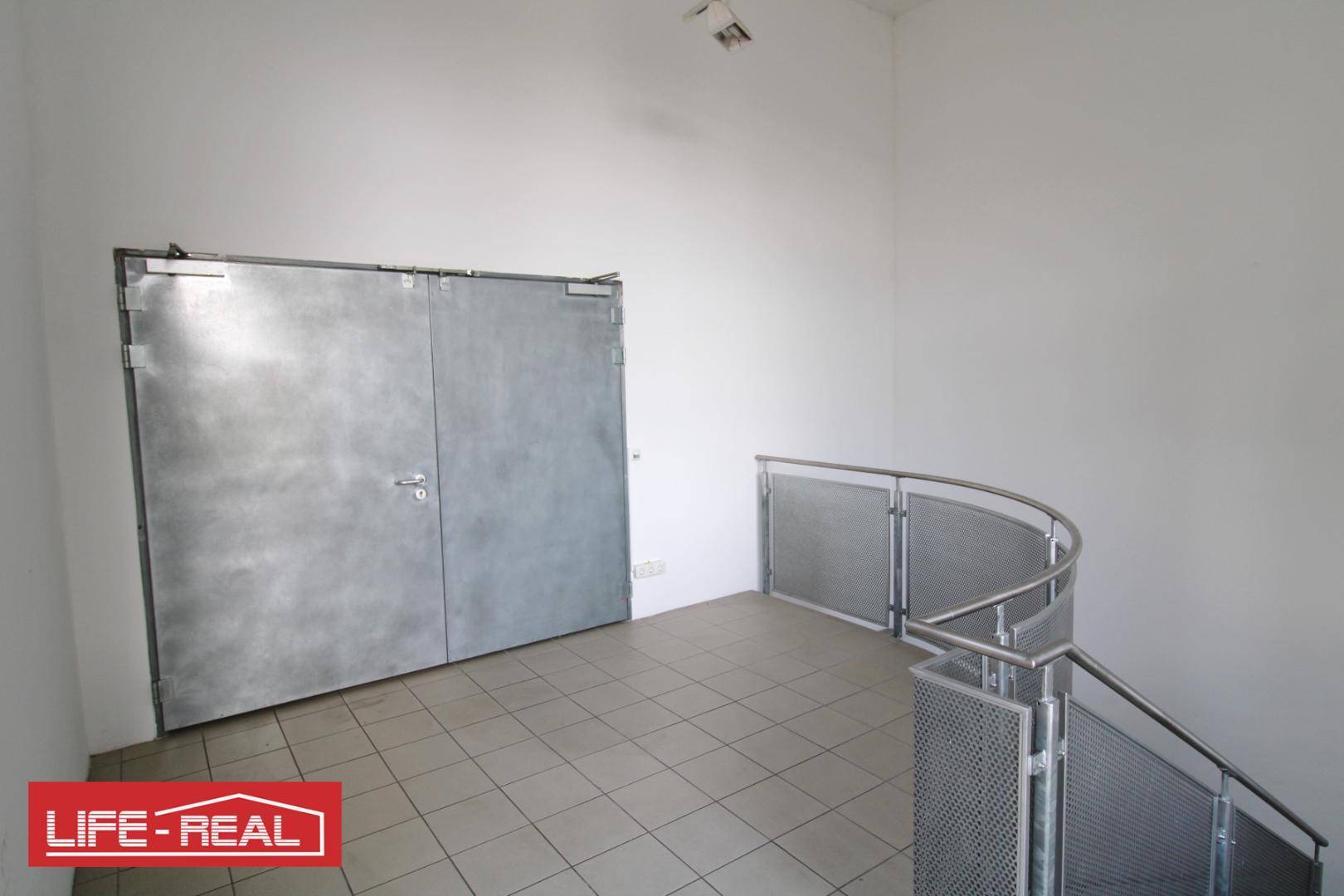 Treppenhausbereich mit gefliestem Boden, Metallgeländer und großen Doppeltüren.