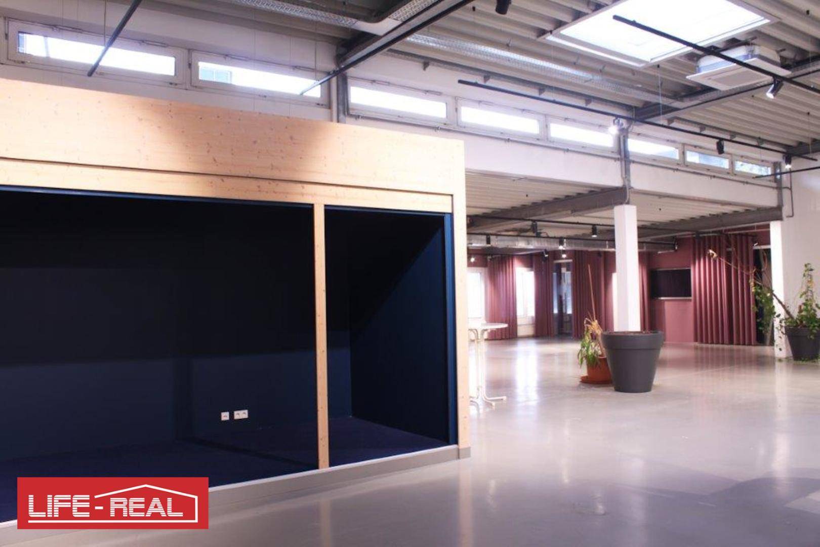 Großer Gewerberaum mit hohen Decken, Betonboden und einer eingebauten Holzkabine mit dunklem Interieur.