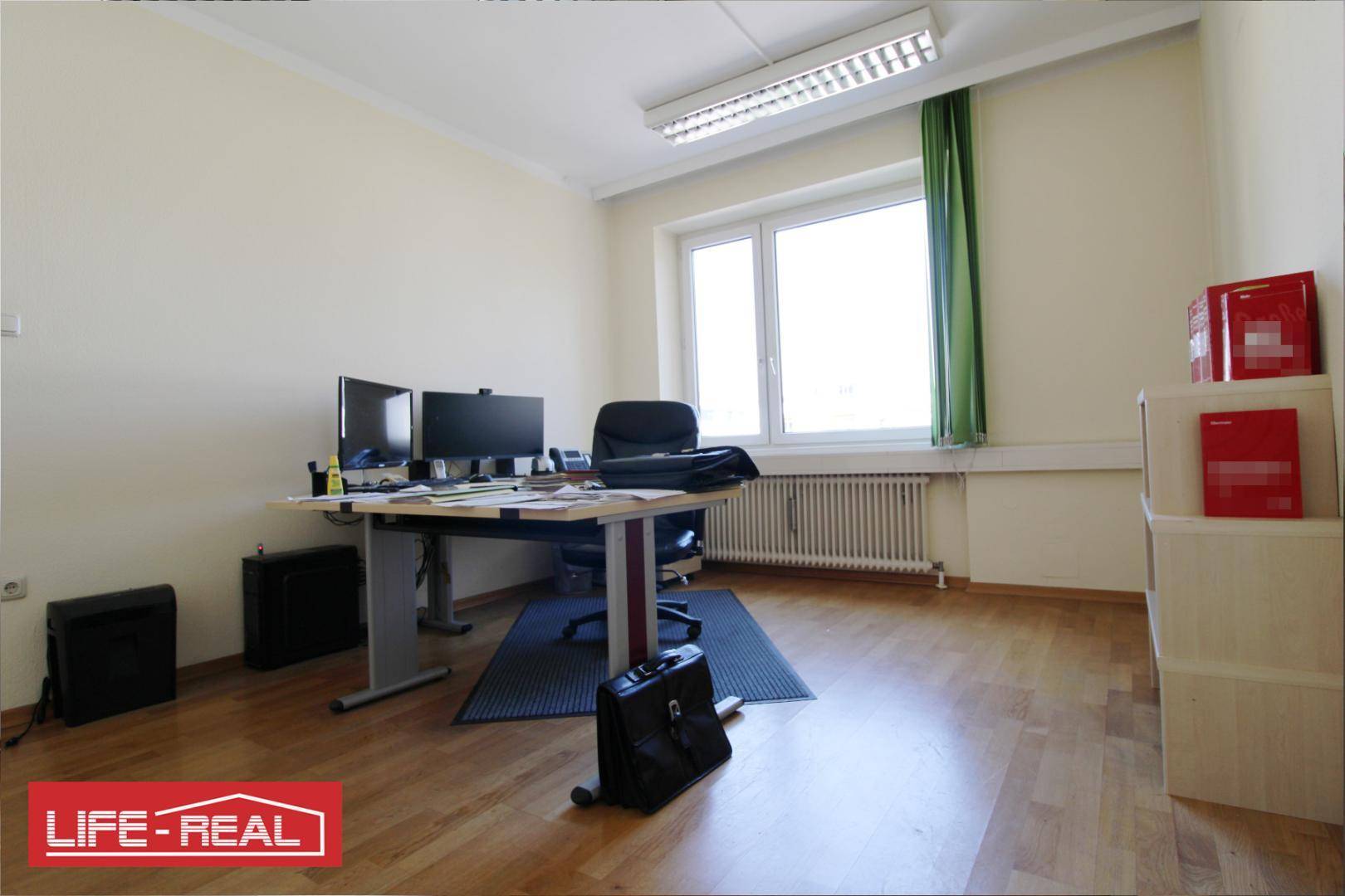 Geräumiges Büro mit zwei Monitoren auf dem Schreibtisch und einem großen Fenster.