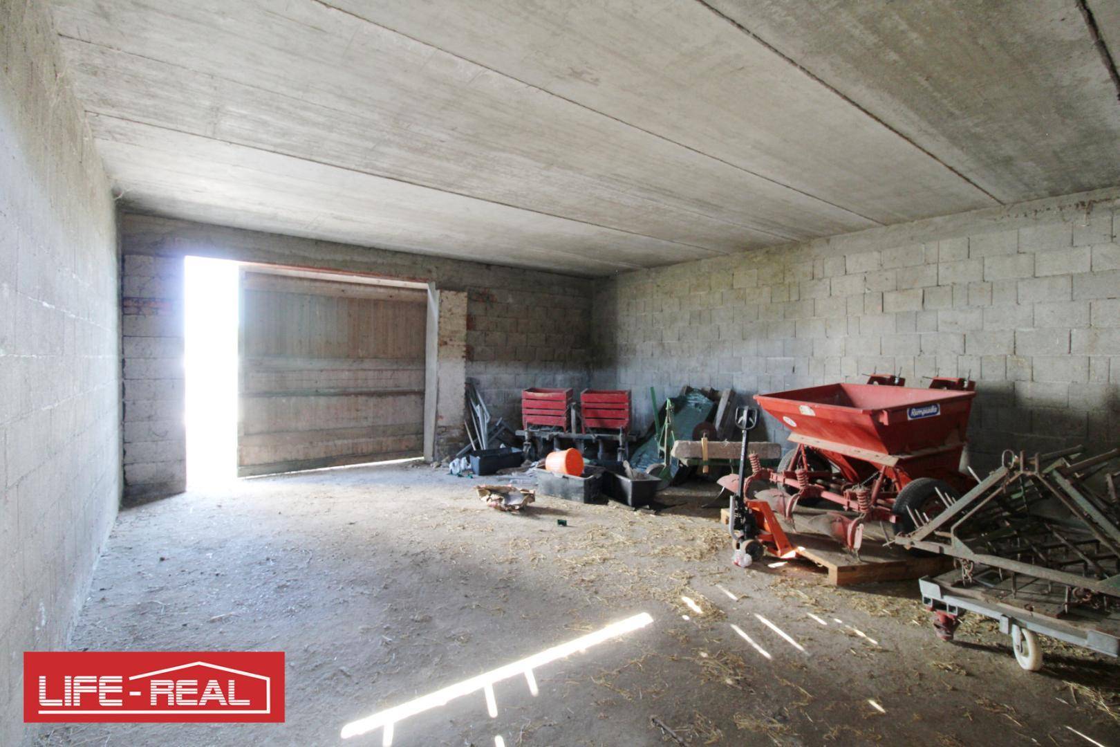 Geräumiger Lagerraum mit Betonwänden, Holztüren und verschiedenen landwirtschaftlichen Maschinen im Inneren.
