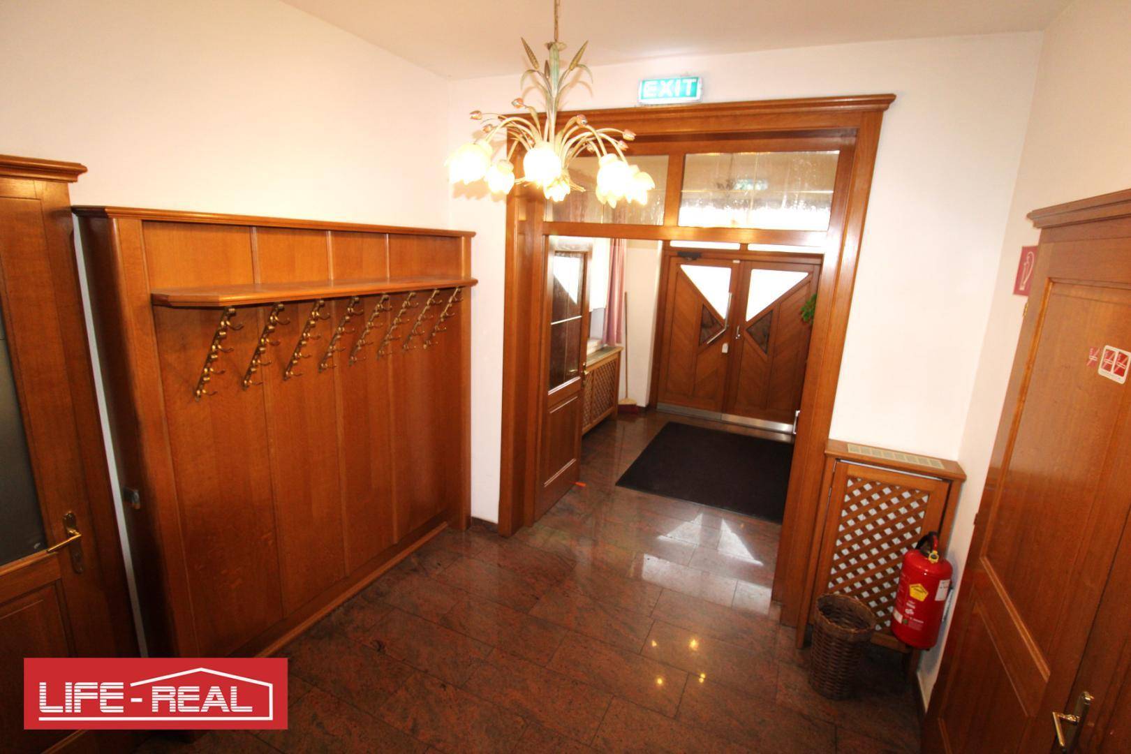 Eingangsbereich mit dunklem Holzvertäfelung, Garderobe und einem klassischen Kronleuchter, der den Raum erhellt.