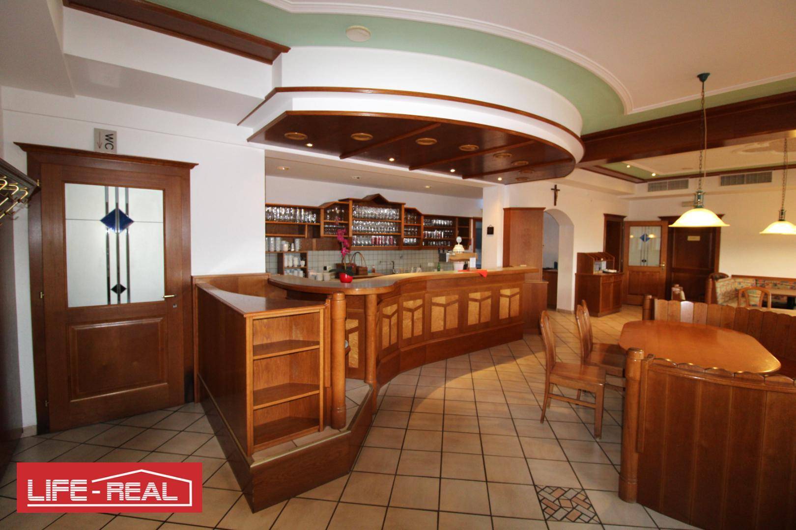 Gemütlicher Restaurantbereich mit einer geschwungenen Holztheke, gepolsterten Sitzbänken und Fliesenboden.