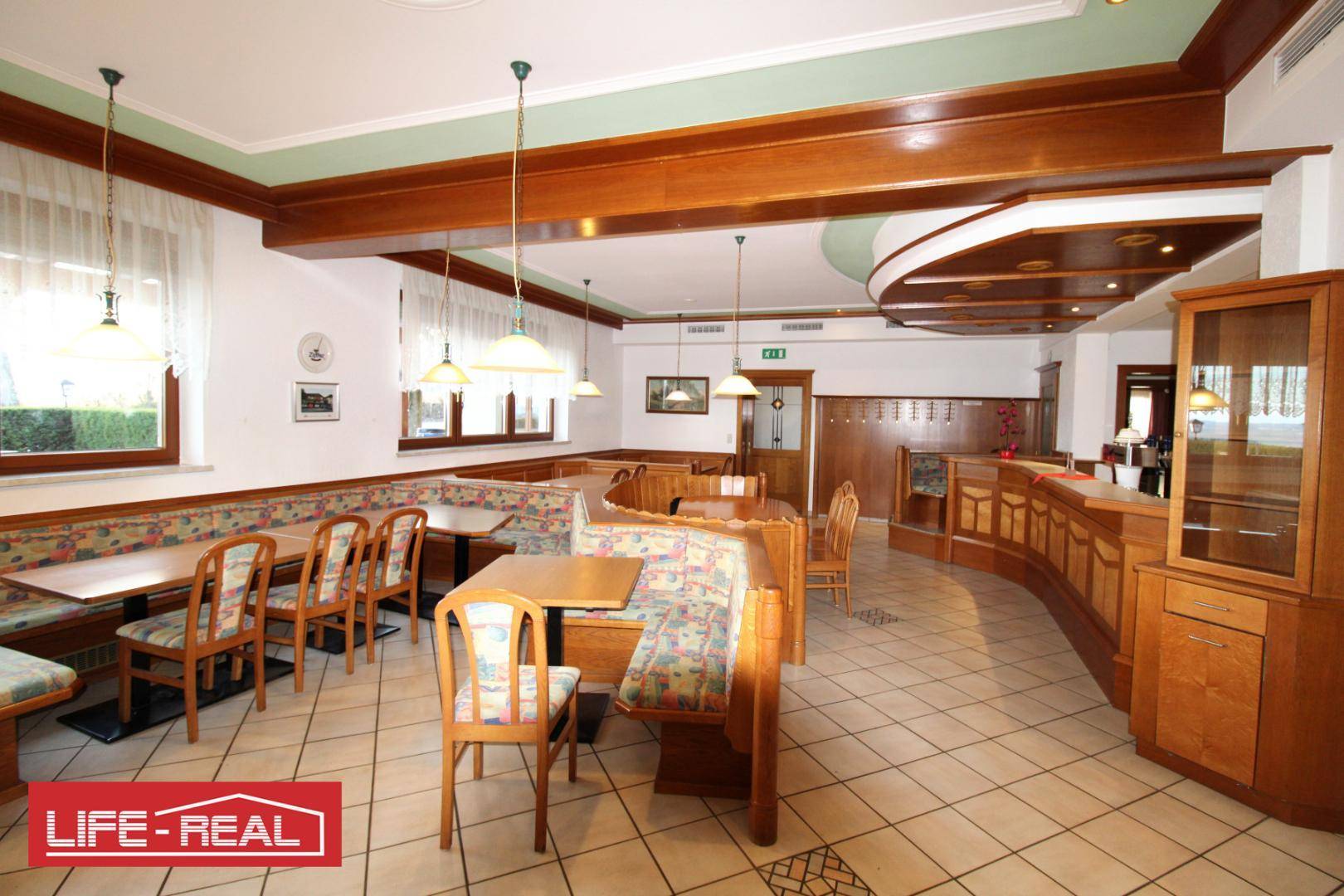Geräumiger Speisesaal mit gepolsterten Holzbänken, Tischen und großen Fenstern, die eine helle Atmosphäre schaffen.