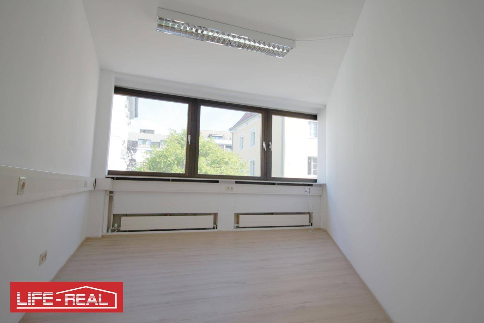 Heller Raum mit großen Fenstern und Holzfußboden, ideal für ein kleines Büro oder Arbeitszimmer.