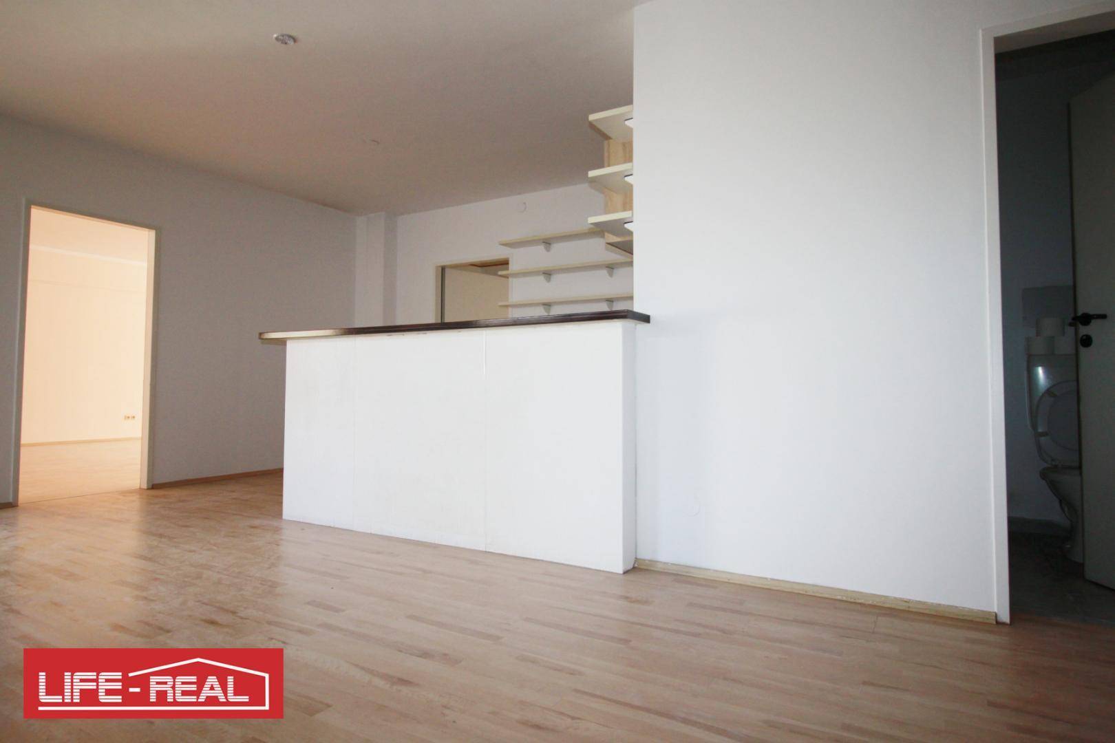 Heller Raum mit Holzfußboden und einer Theke, die als Empfang oder Küchenzeile dienen könnte.