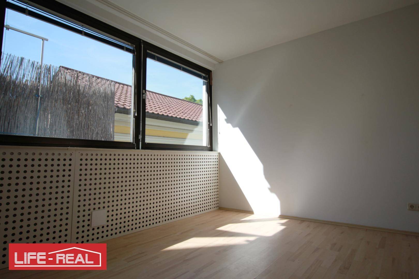 Sonniger Büroraum mit großen Fenstern, die viel Tageslicht hereinlassen und hellem Boden.