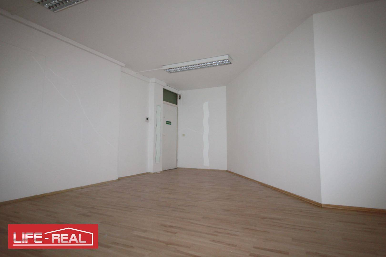 Leerer Büroraum mit Laminatboden und einer Tür, die zu einem anderen Bereich führt.