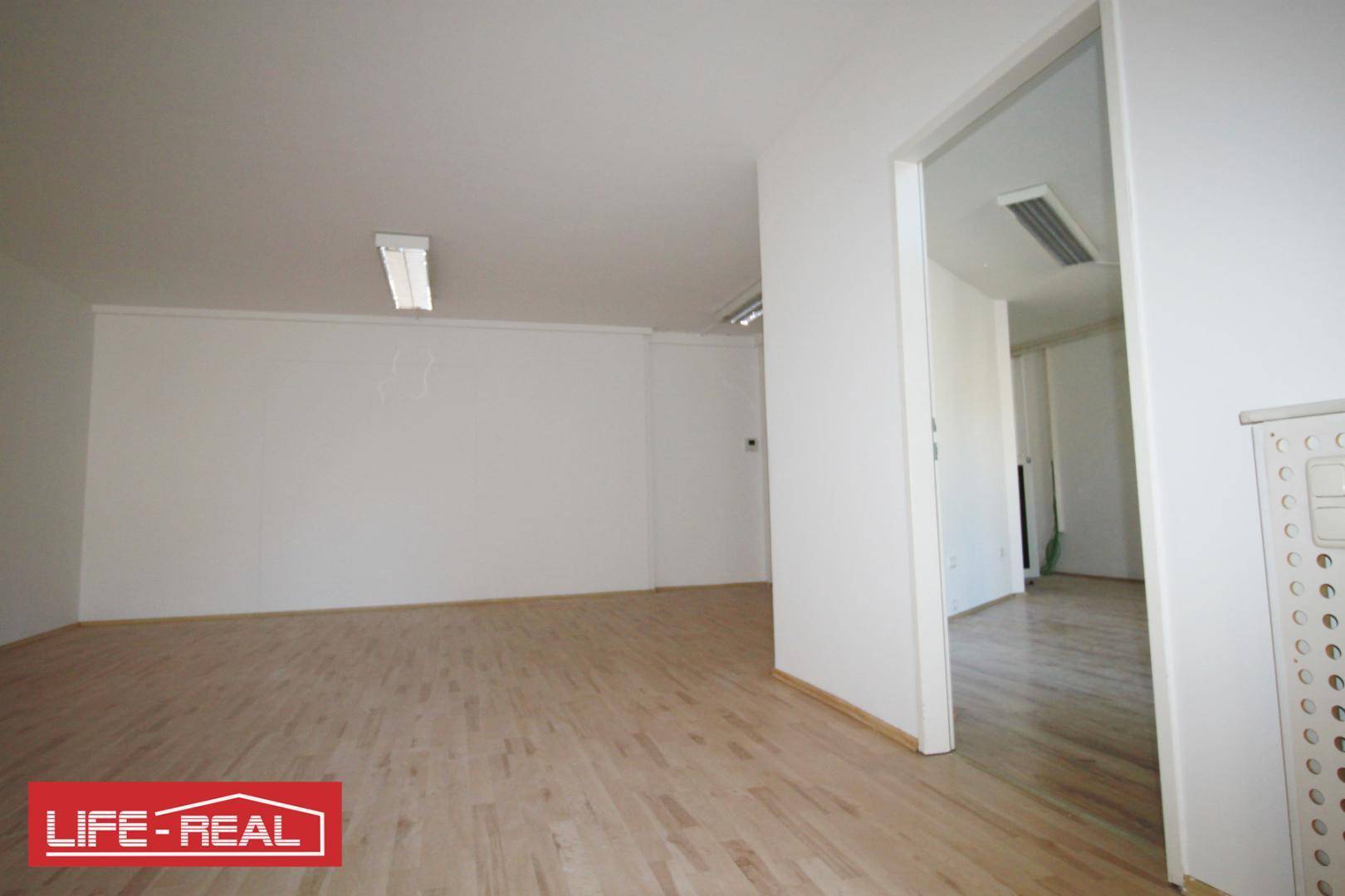 Heller Büroraum mit Laminatboden und Zugang zu einem weiteren Zimmer.