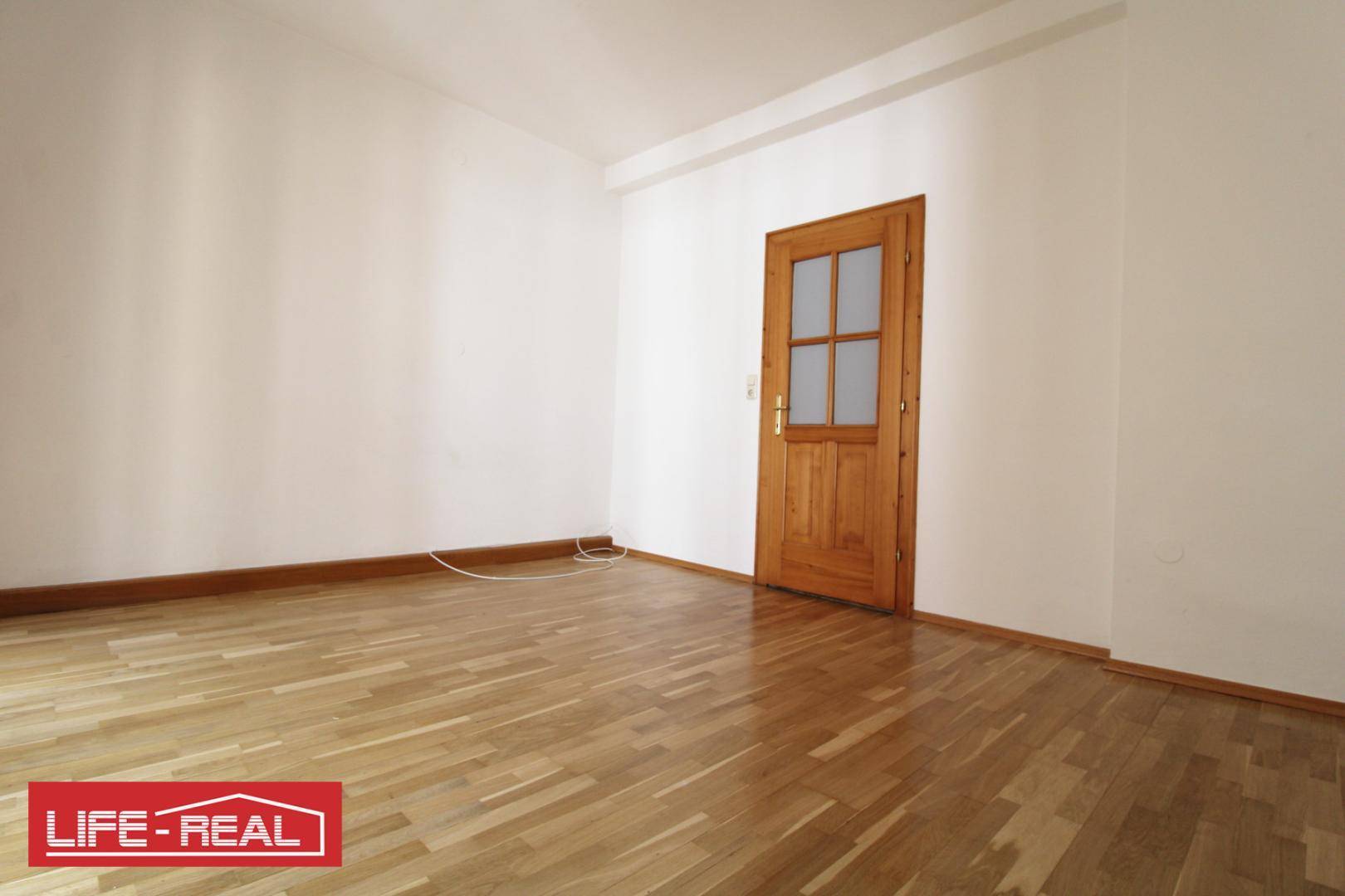 Leerer Raum mit hellem Parkettboden und einer Holztür, bereit für neue Einrichtungsideen.