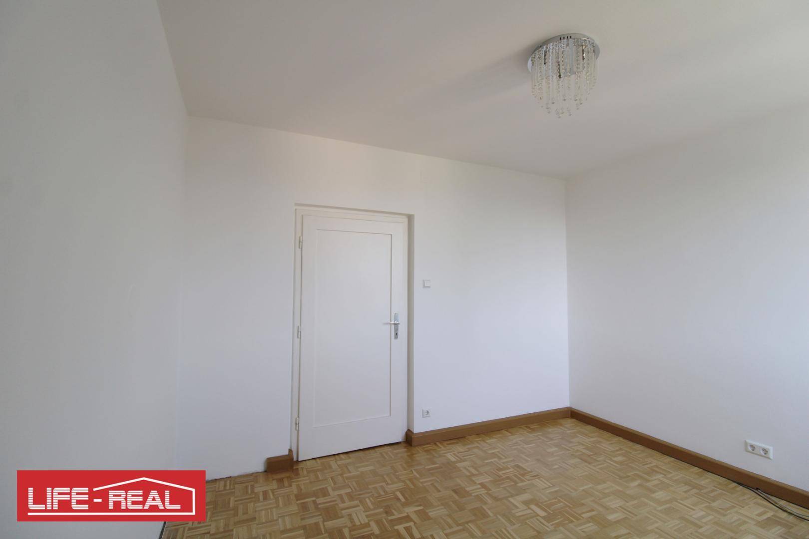 Schlichtes Zimmer mit Parkettboden und weiß gestrichenen Wänden.